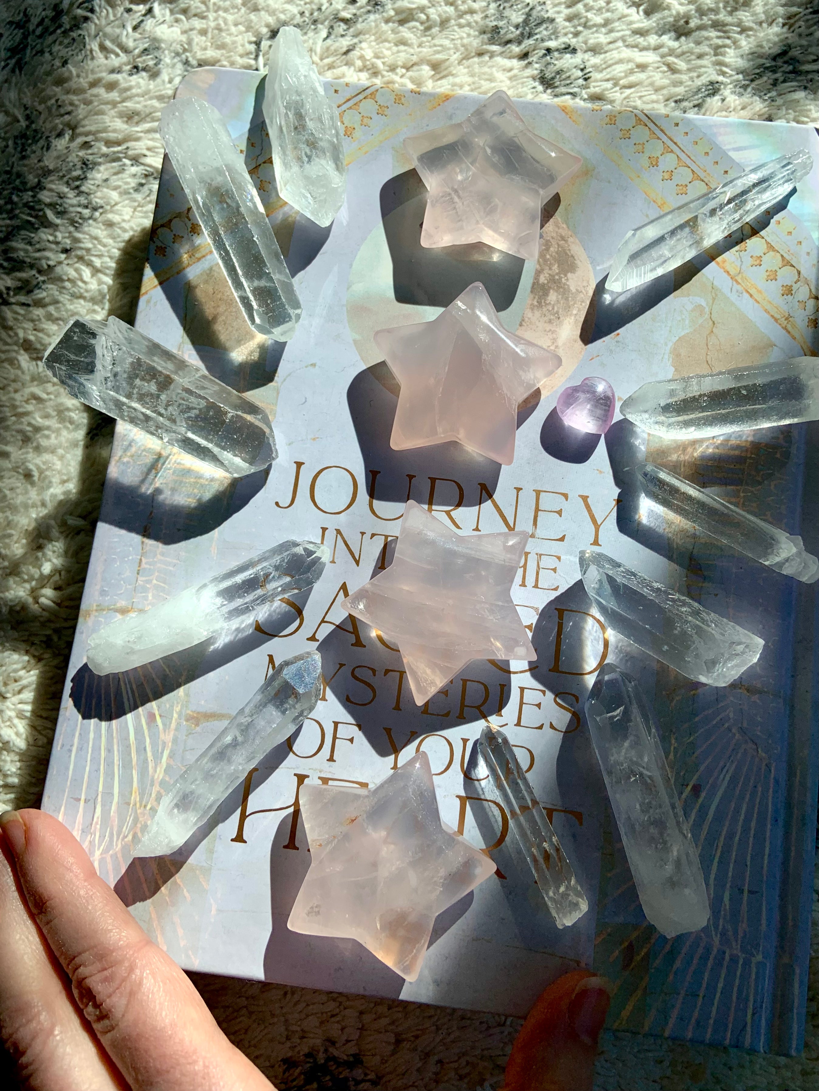 large rose quartz crystal stars with clear quartz points in a sunlit crystal grid on book for heart chakra healing décor