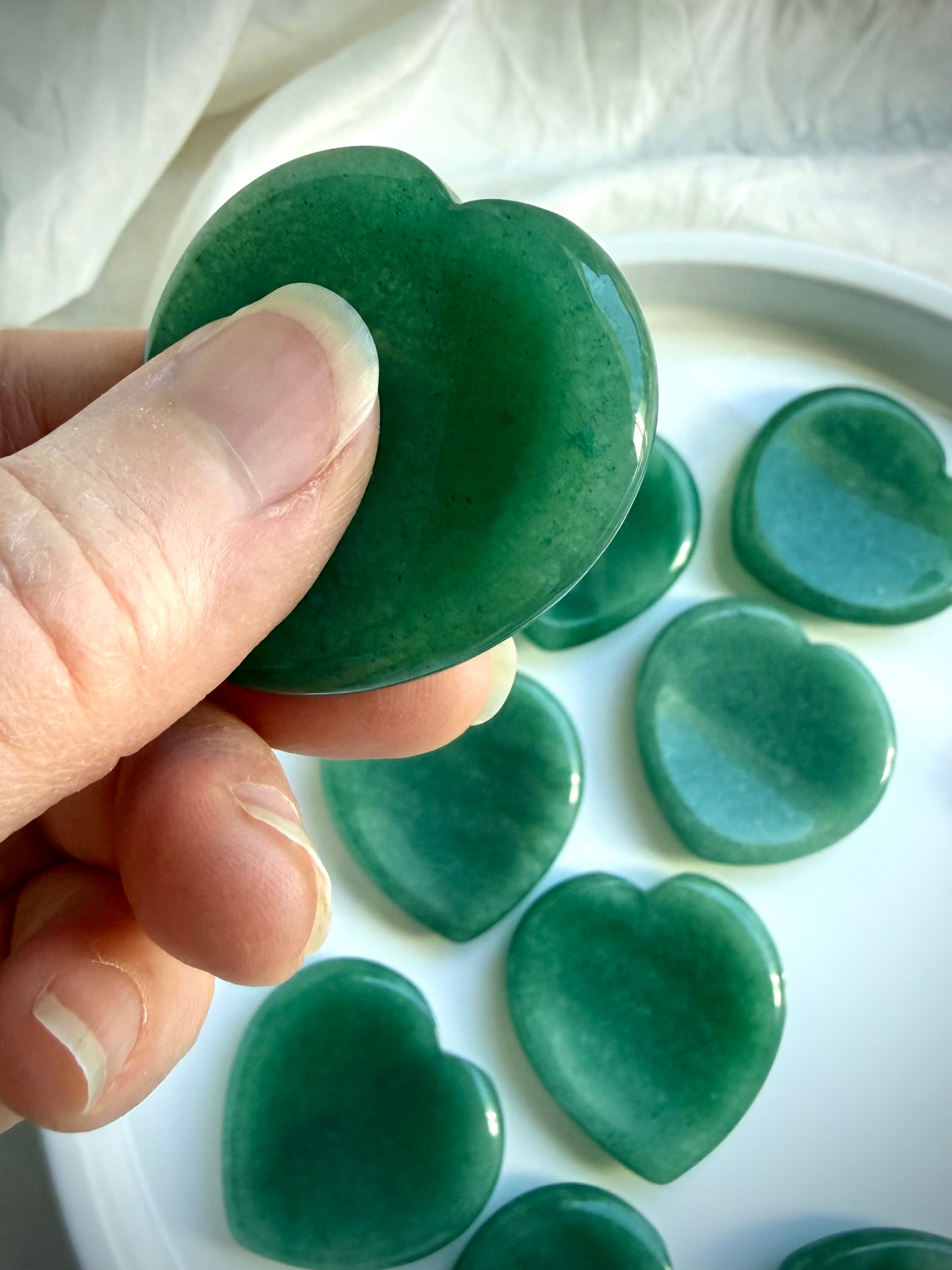 green aventurine heart crystal held between fingers with natural mineral patterns for growth and heart chakra healing