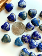 Close-up of Mini Lapis Lazuli heart carvings show with a US quarter for scale, rich blue color, calcite marbling, and subtle pyrite flecks in polished stone