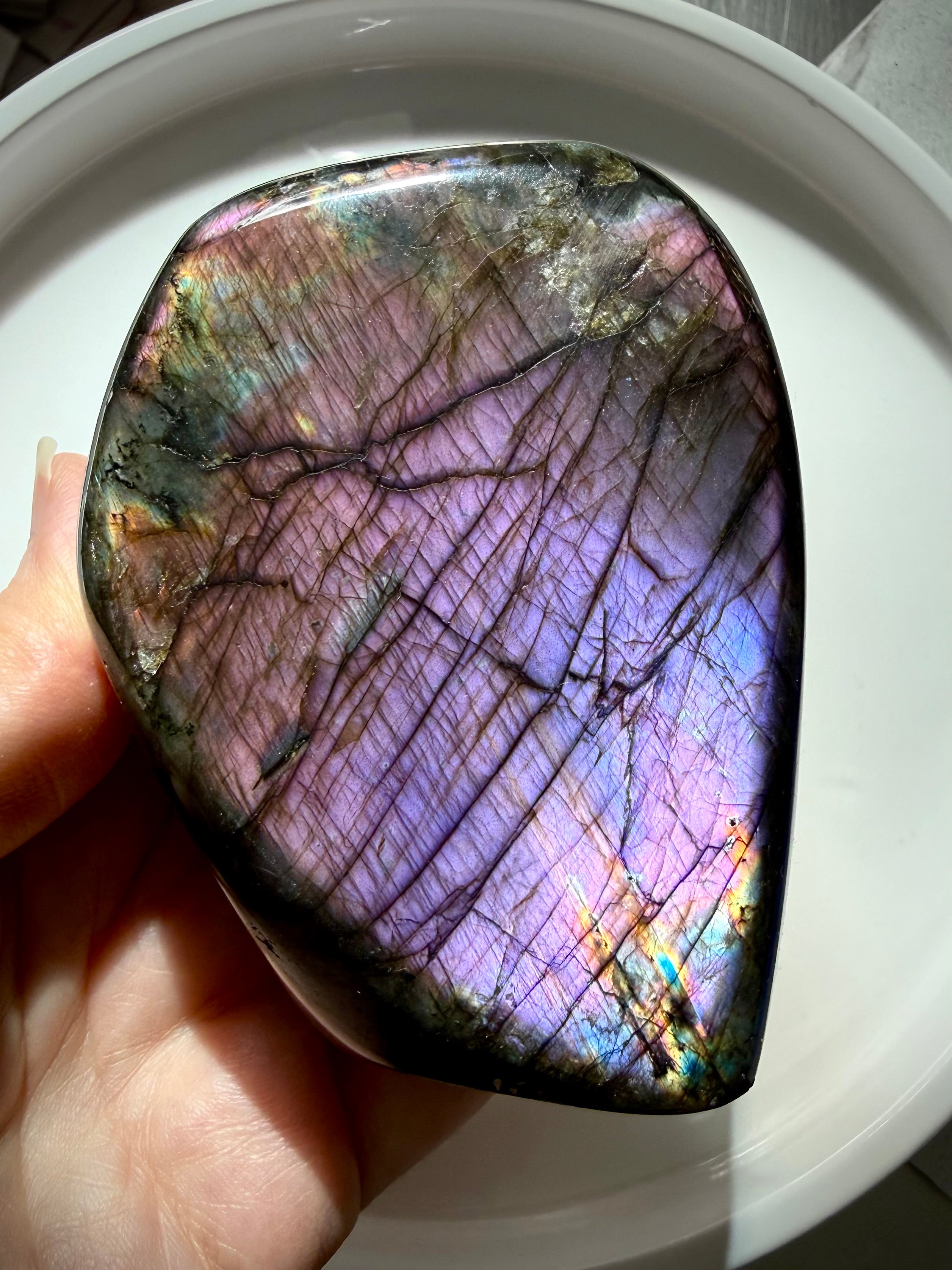 Pastel Labradorite crystal held in hand with soft pink, purple and lavender flash shifting across the polished face