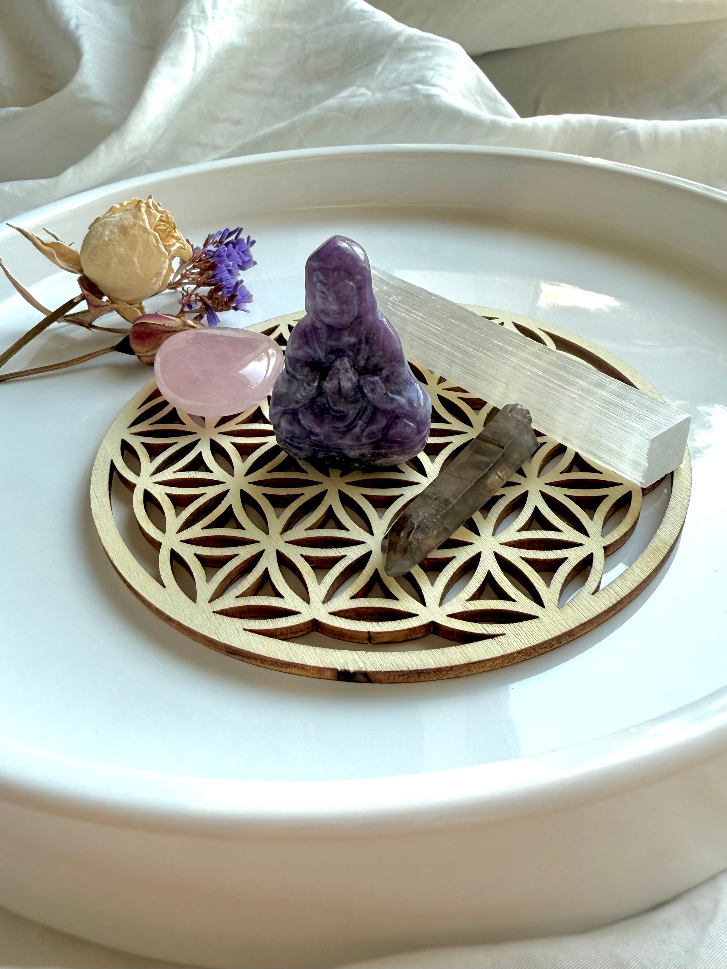 Crystal altar setup featuring lepidolite Quan Yin, rose quartz, smoky quartz, and selenite wand on flower of life grid