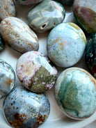 Close-up of polished Sea Jasper palm stones featuring orbicular patterns, druzy pockets, agate banding, and soft teal, pink, and gray tones