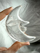 Clear Quartz Moon Face carving held in natural light, revealing exceptional clarity, smooth glossy polish, and celestial design
