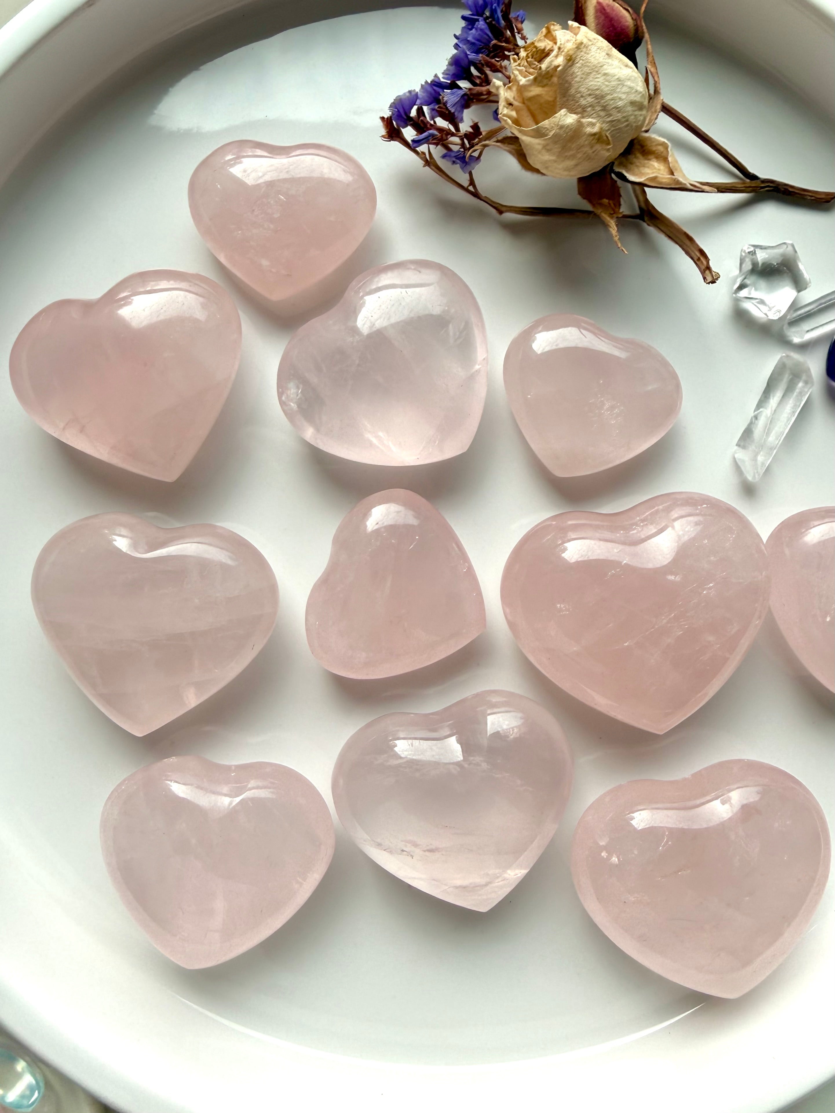 Polished rose quartz crystal hearts arranged on a tray, soft pink stones for self love and heart chakra healing