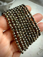 close up of stacked pyrite bracelets in hand highlighting faceted sparkle and metallic luster