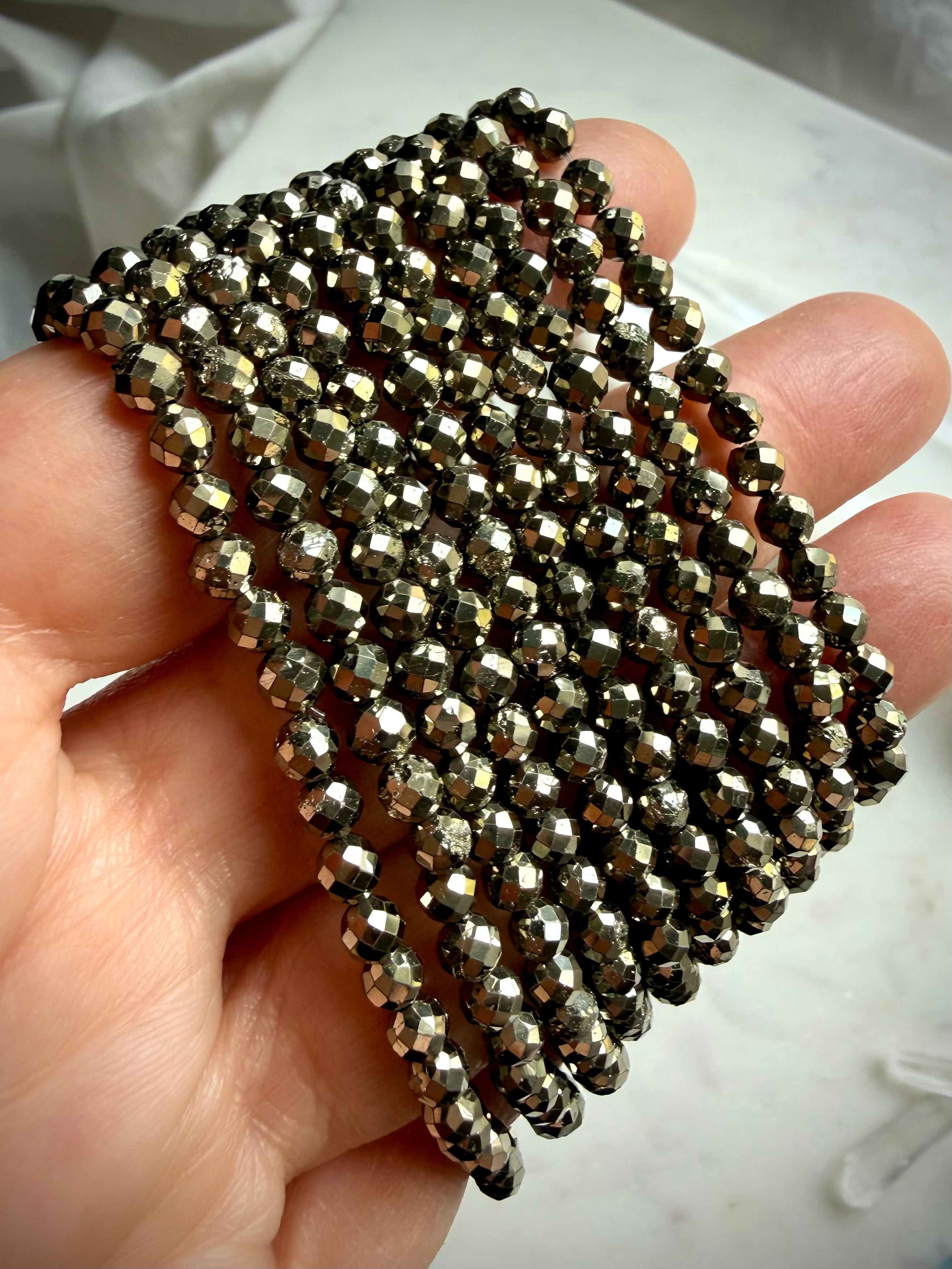 close up of stacked pyrite bracelets in hand highlighting faceted sparkle and metallic luster