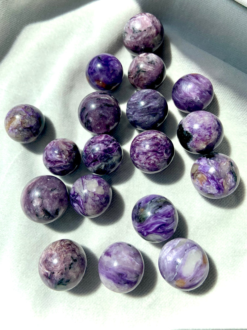 An array of Purple Charoite mini spheres photographed in bright natural light on a light background