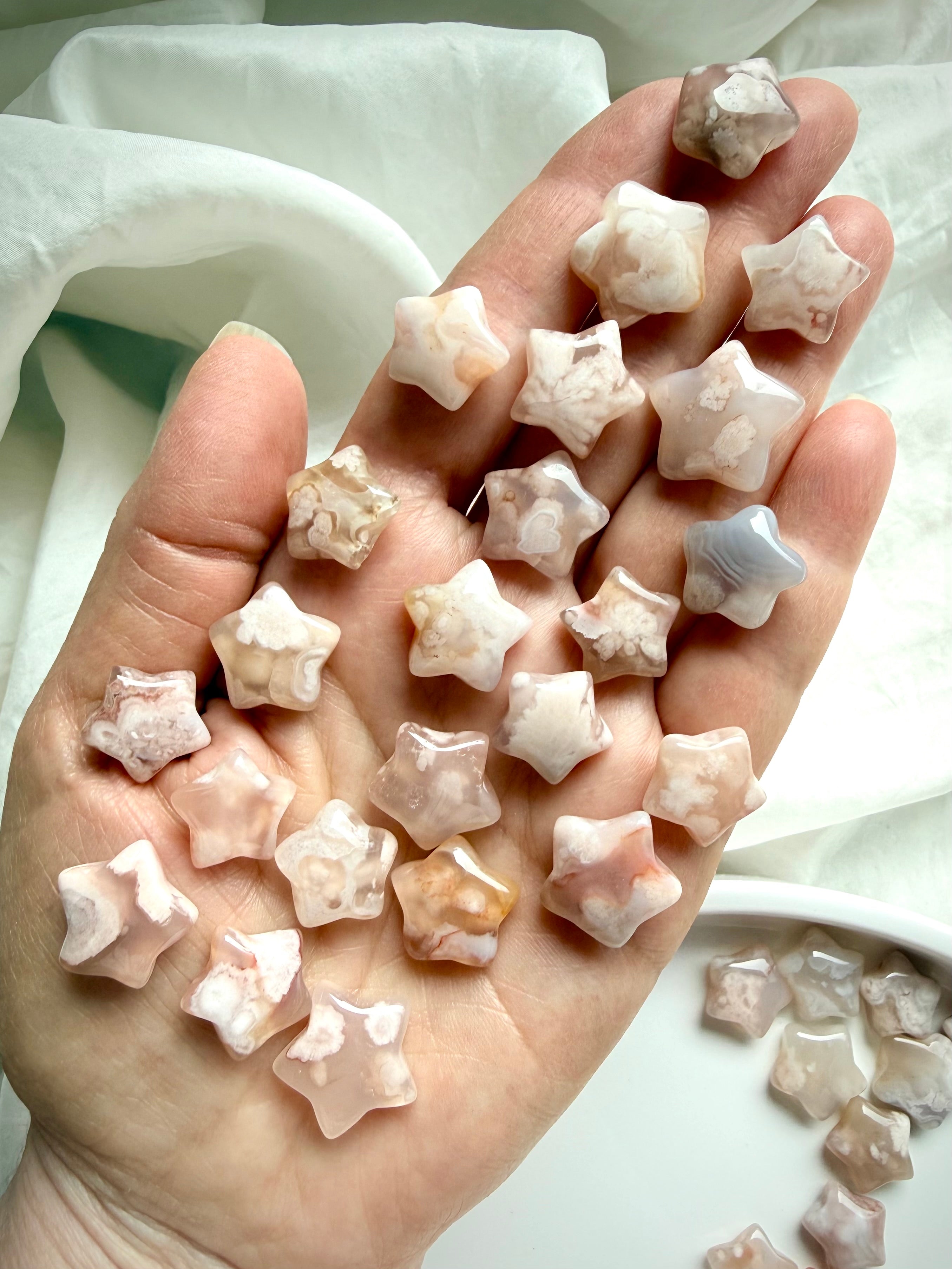Hand holding mini Flower Agate star carvings with floral inclusions and dreamy pastel chalcedony tones