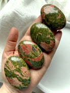 Unakite palm stones resting on hand polished crystal set with green and pink tones for heart chakra healing and emotional balance