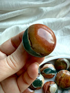 Closeup of a mini Polychrome Jasper palm stone with earthy green, terracotta, gray & cream patterns