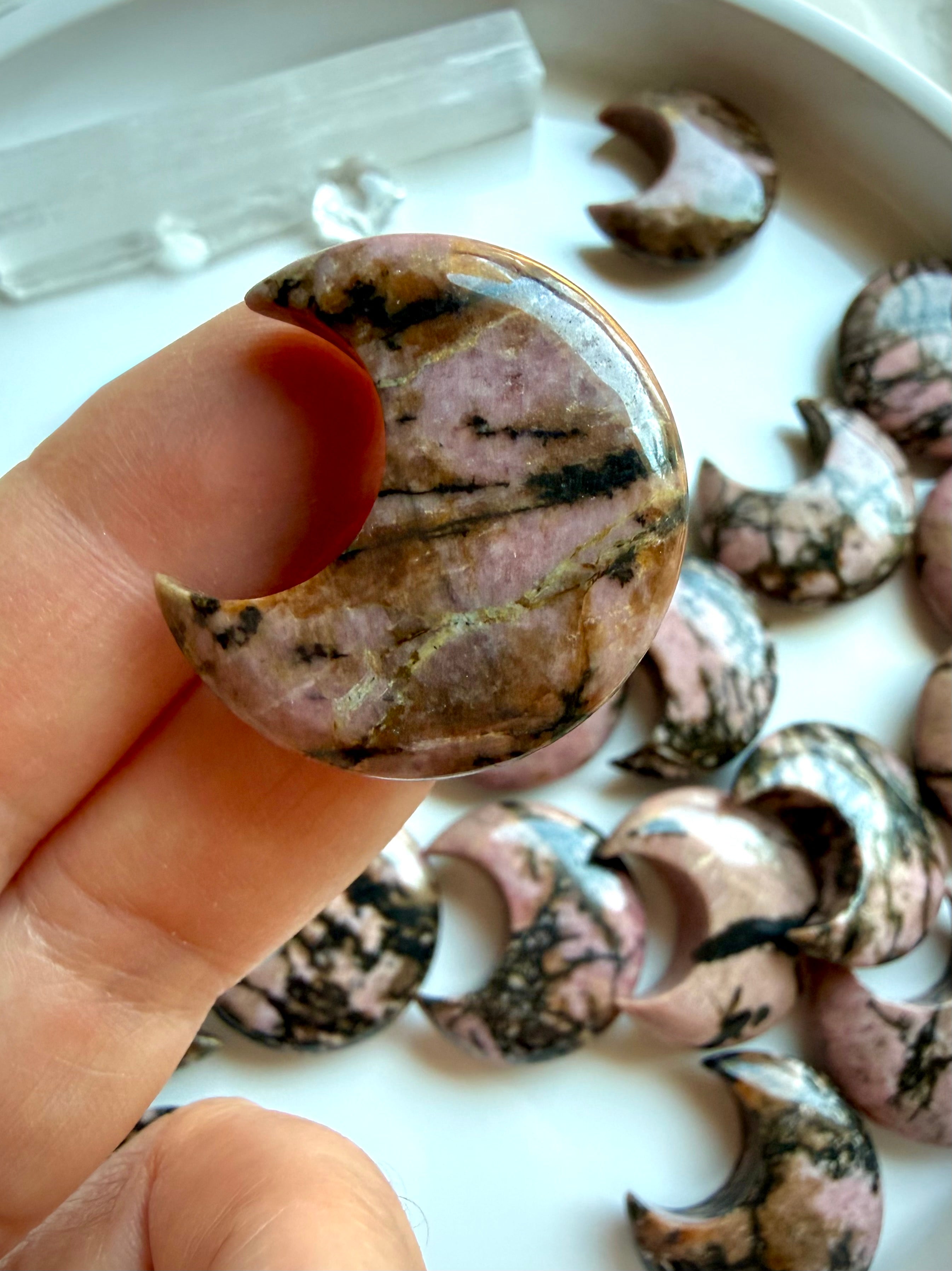 Close-up of a polished Rhodonite moon carving highlighting natural black manganese veining and soft pink color