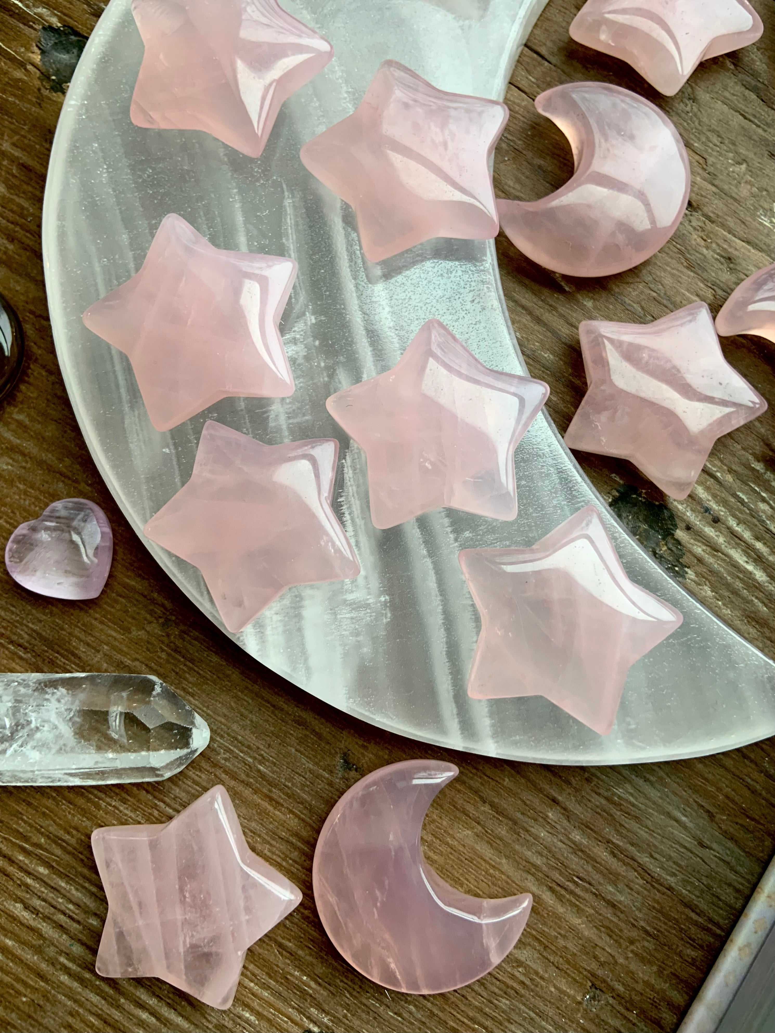 Closeup of rose quartz moons and stars on a white moon plate, styled on dark wood. Healing crystals for love & tranquility.