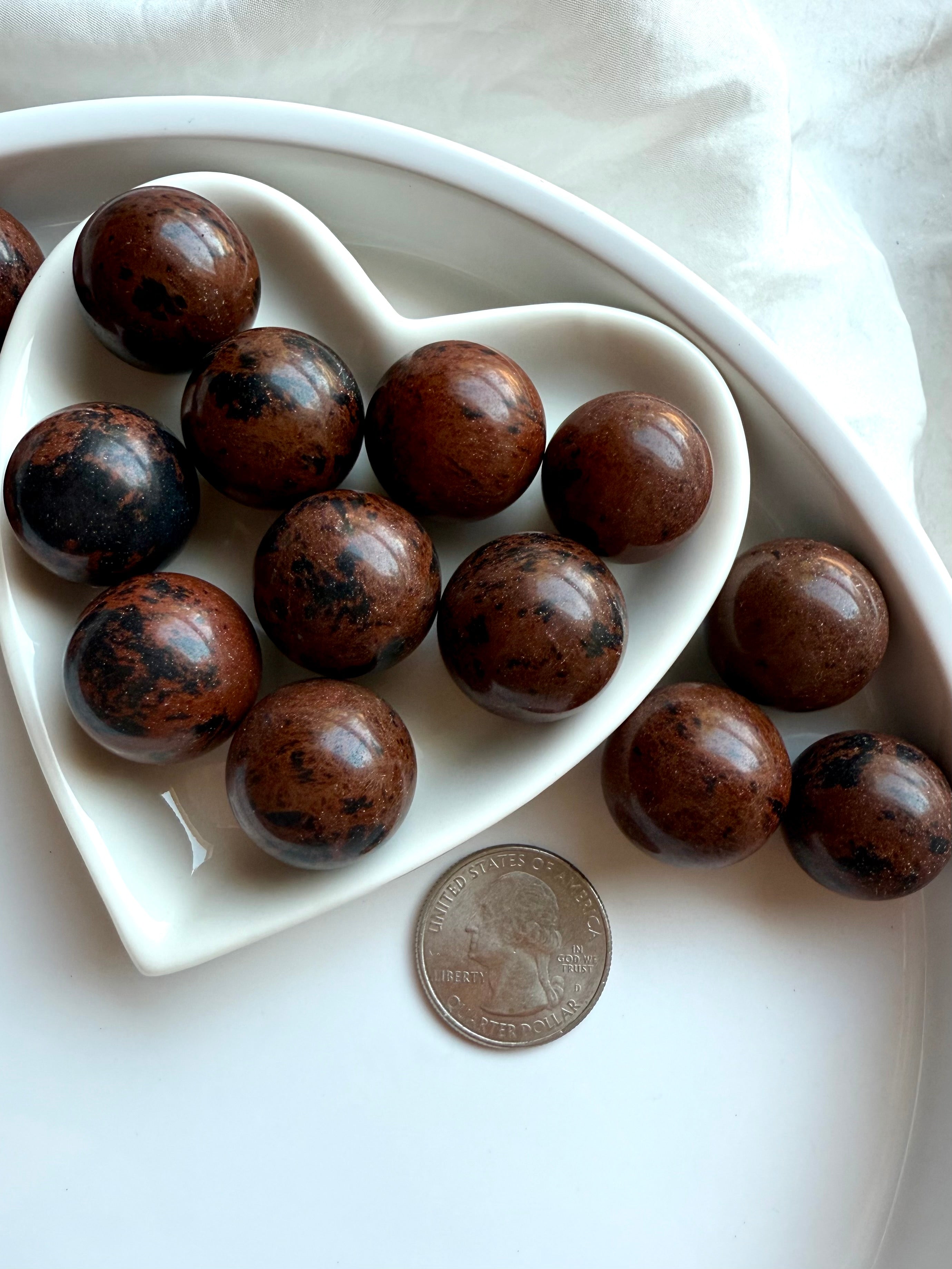 Small Mahogany Obsidian spheres in white heart dish with quarter for size reference – healing crystals for grounding