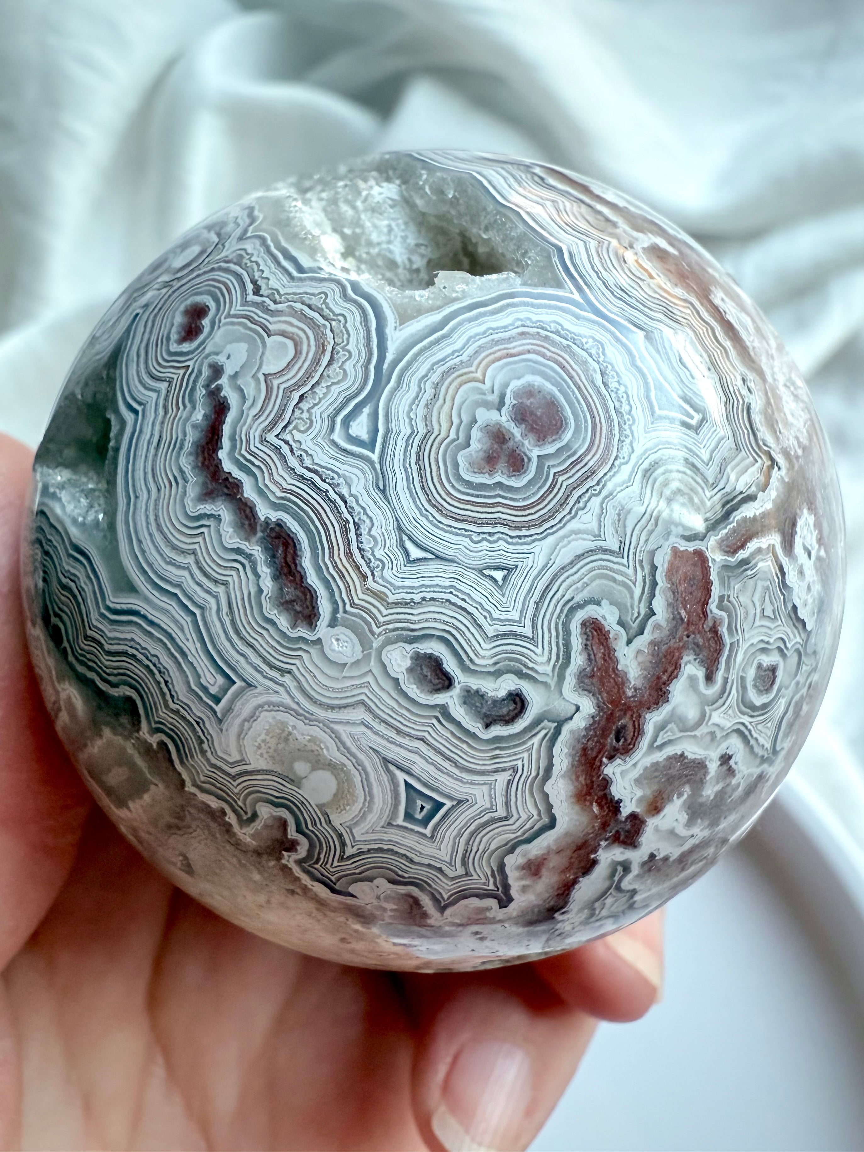 Detailed view of unique lace agate orb featuring bullseye patterns and geode inclusions, hand holding sphere