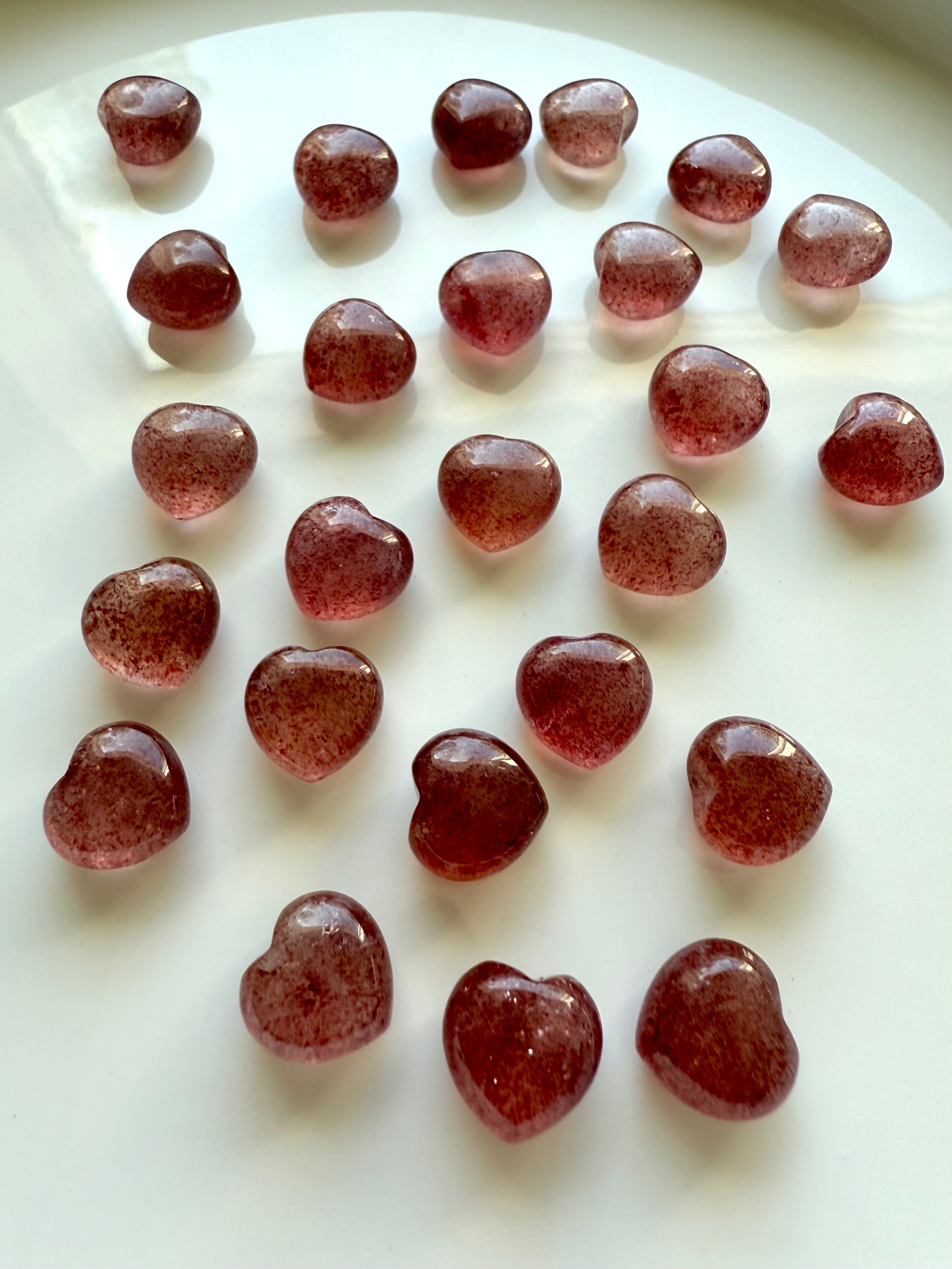 Angled view of Strawberry Quartz mini hearts arranged on a white background — pocket-sized tanzberry quartz carvings.
