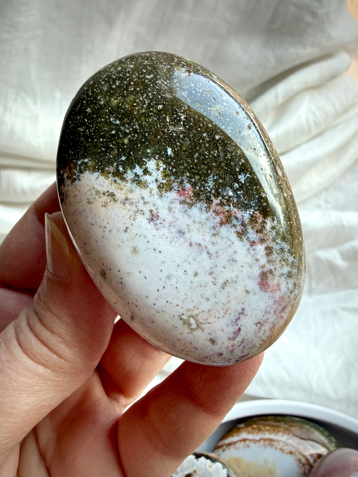 Close up of an Ocean Jasper palm stone in shades green, and white with orbicular mineral patterns
