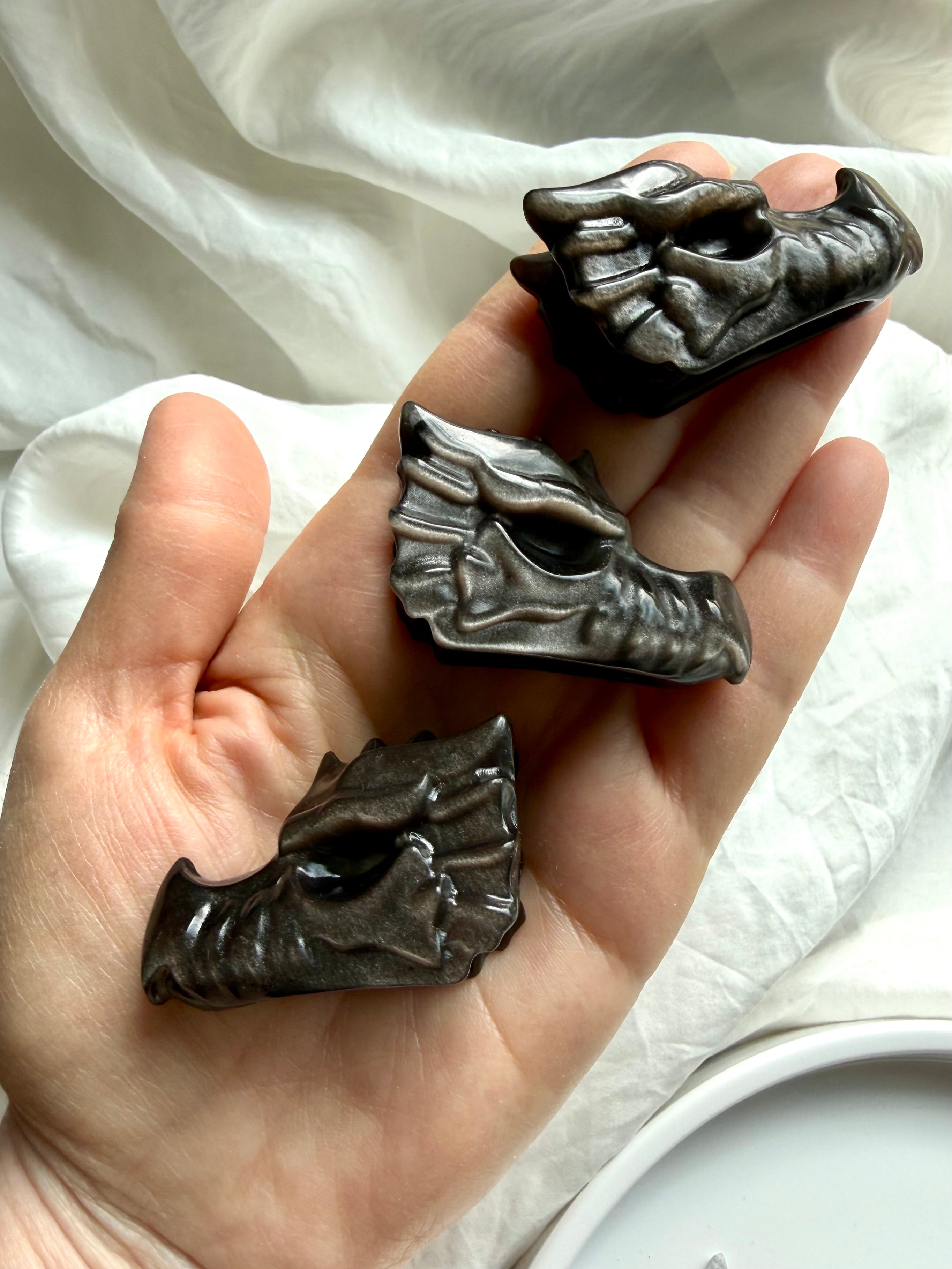 hand holding three silver sheen obsidian dragon carvings showing detailed carved texture, protective crystal for strength and transformation