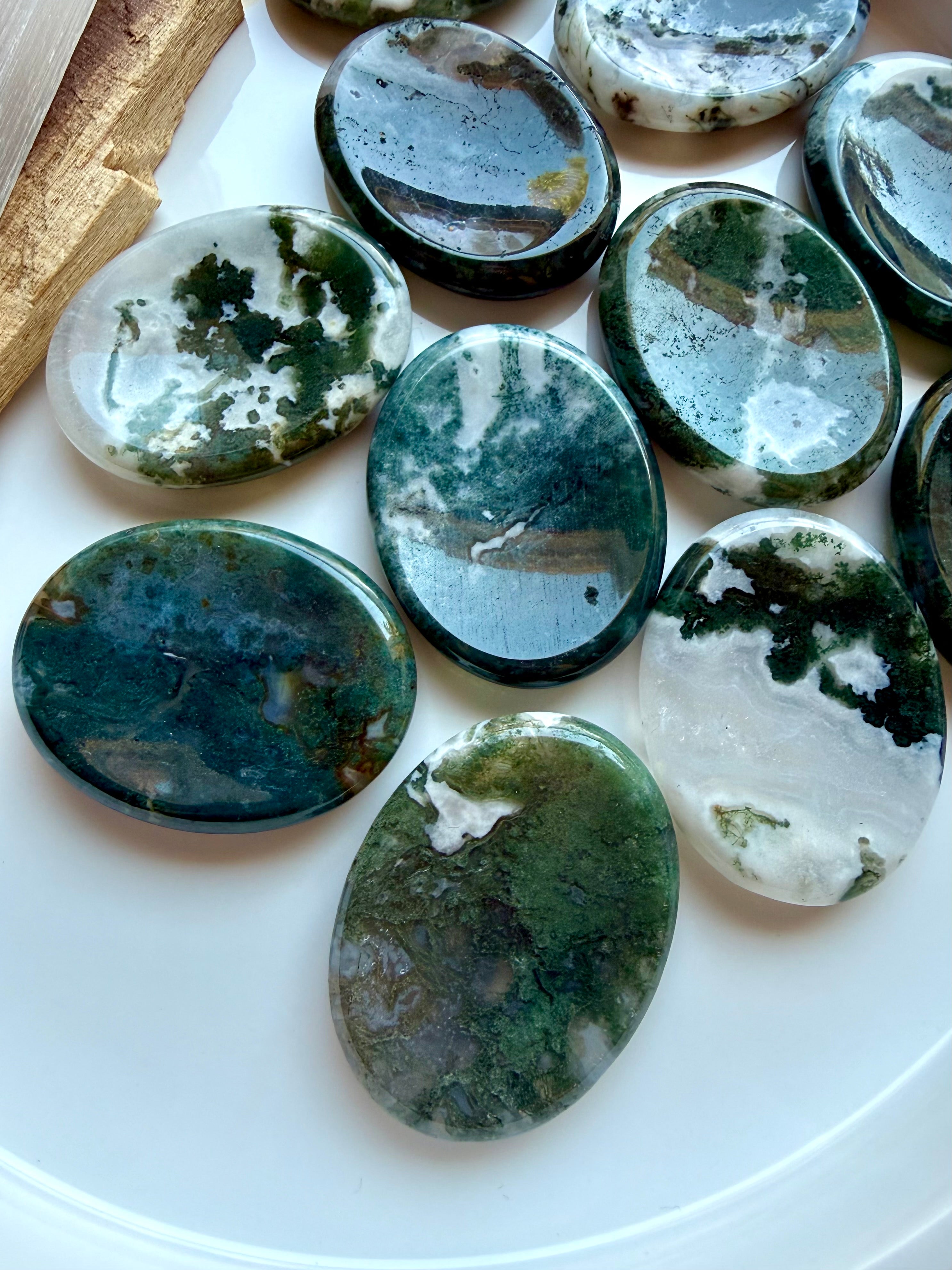 Assorted Moss Agate oval worry stones displayed on a white plate with natural moss patterns and polished finish