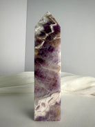 Polished Dream Amethyst tower standing upright, featuring rich purple crystal formations, white quartz chevrons and natural smoky tones