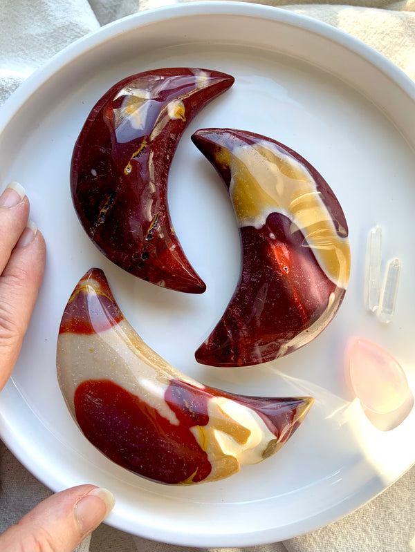 Palm sized, hand carved Mookaite Jasper Crescent Moons shown on a white background with my hand for scale. Choose your favorite!