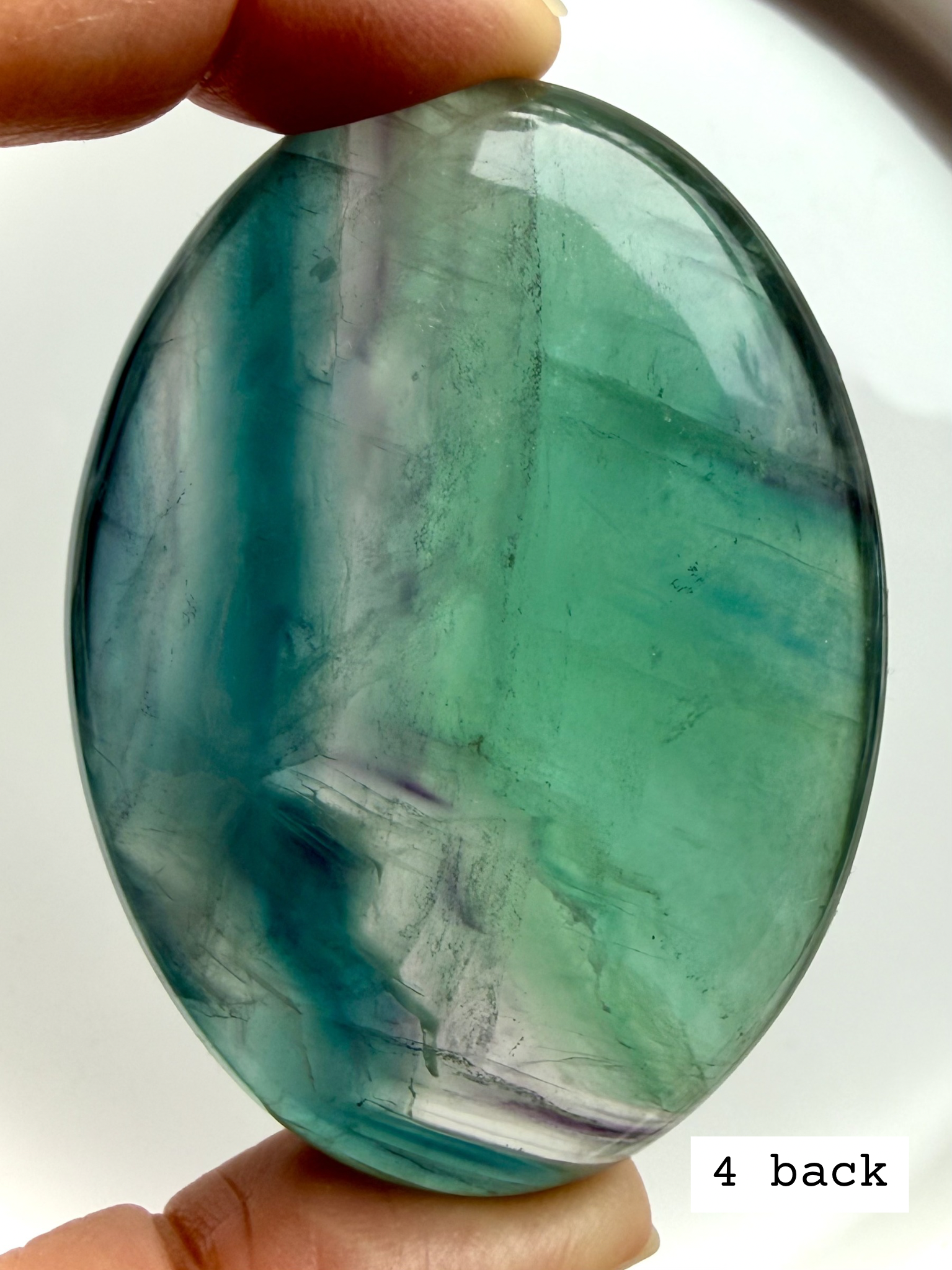 Teal fluorite palm stone #4 back held to the light, displaying translucent blue green bands and mineral variation