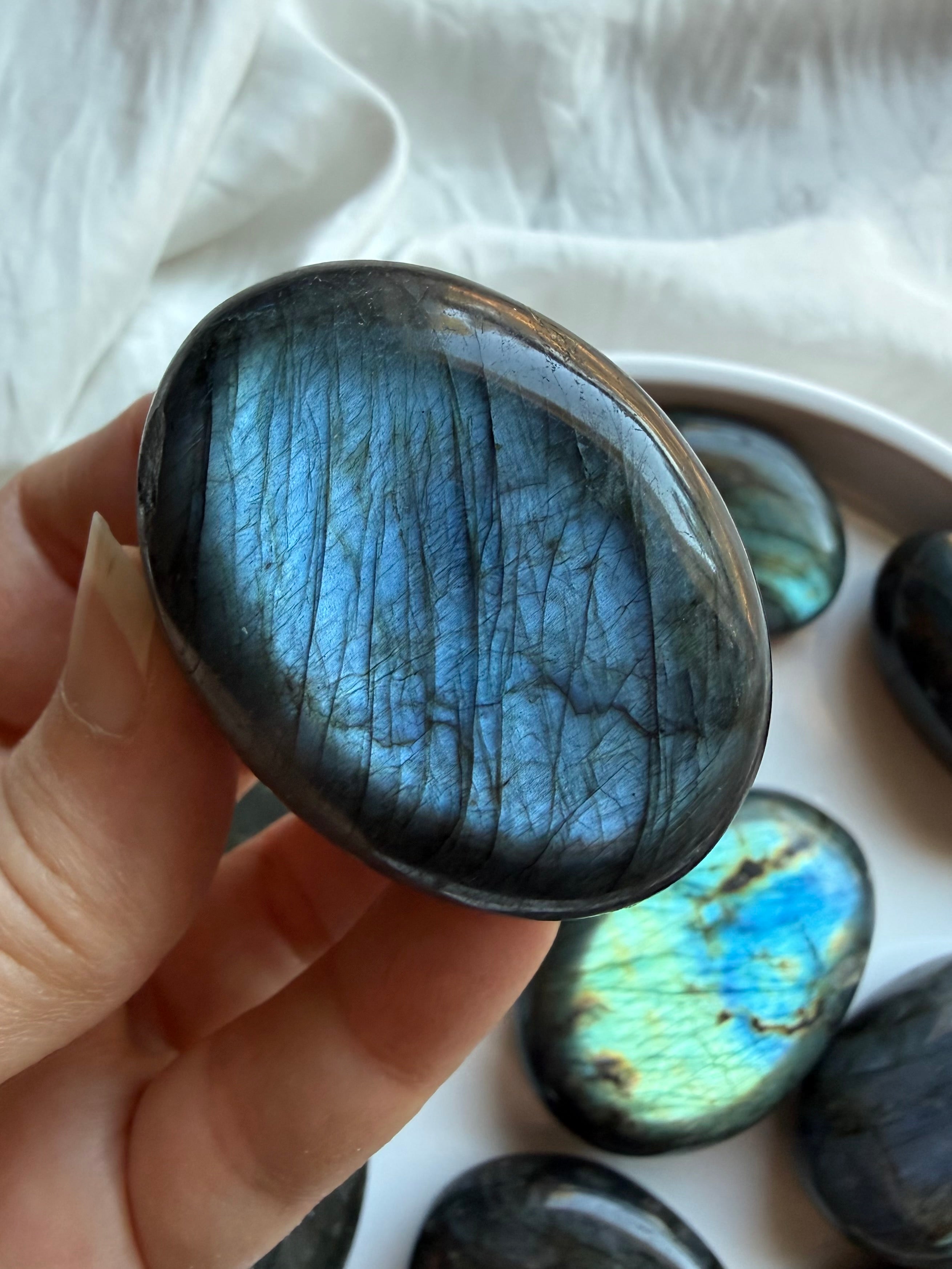 Deep blue flash Labradorite palm stone held in hand with vibrant natural labradorescence