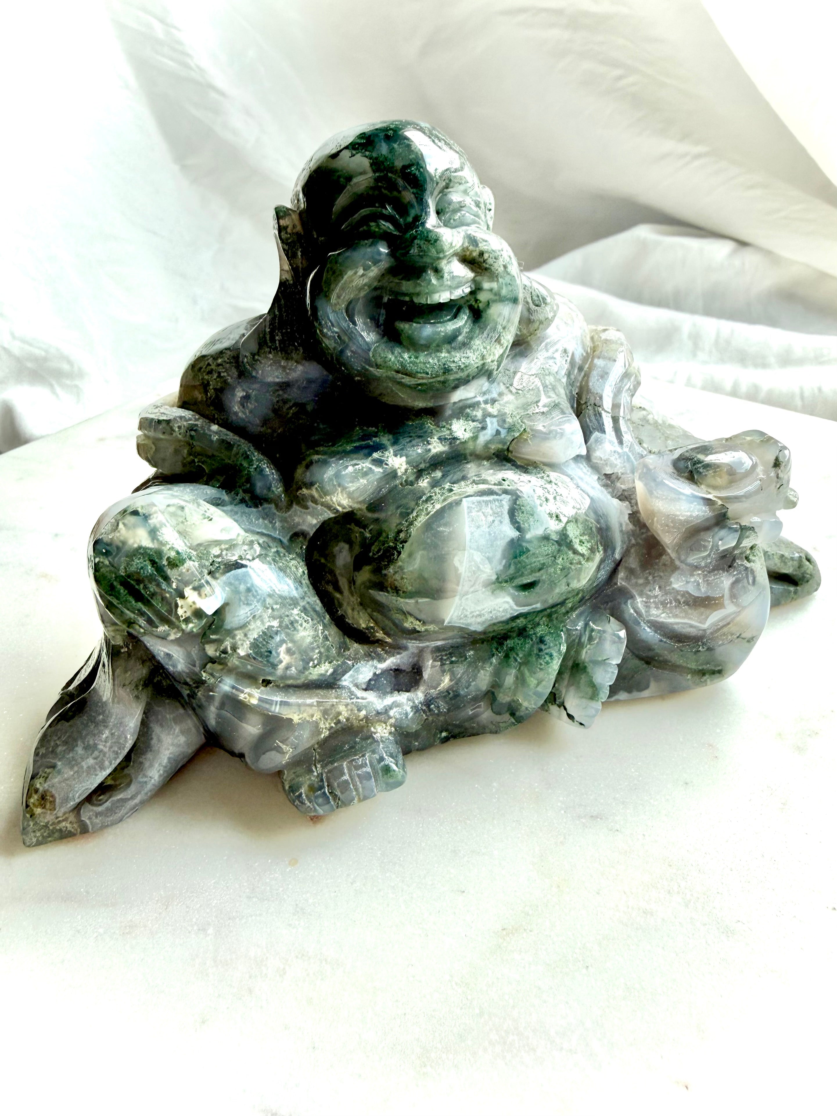Side view of a Large Moss Agate Laughing Buddha crystal carving with translucent Moss Agate