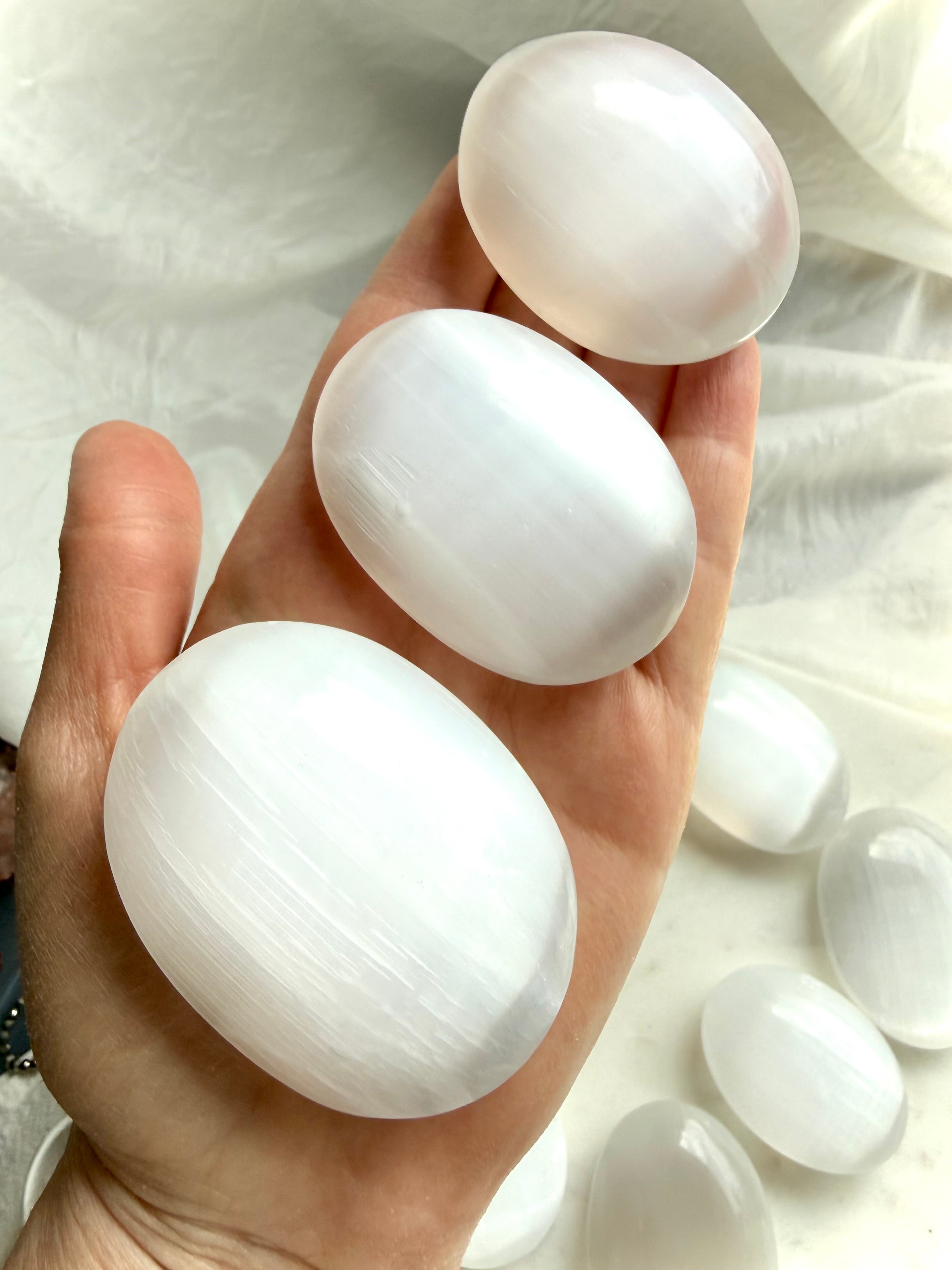Selenite palm stones on hand, used for crystal cleansing, meditation, energy work & peaceful altar decor