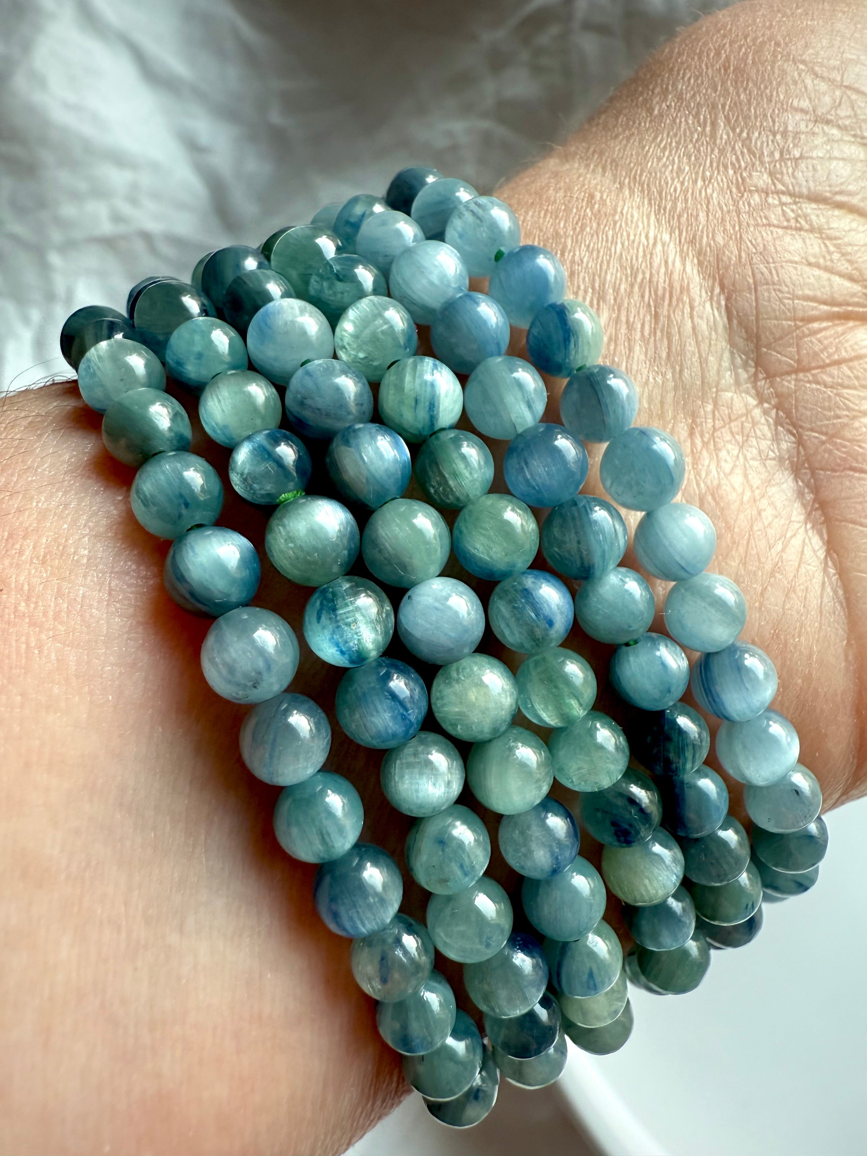 close-up of stacked blue-green kyanite bracelets showing natural silky chatoyance and layered blue tones for throat chakra healing