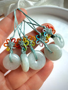 Hand holding five jade peace buckle pendants with colorful macrame knotwork on green cord