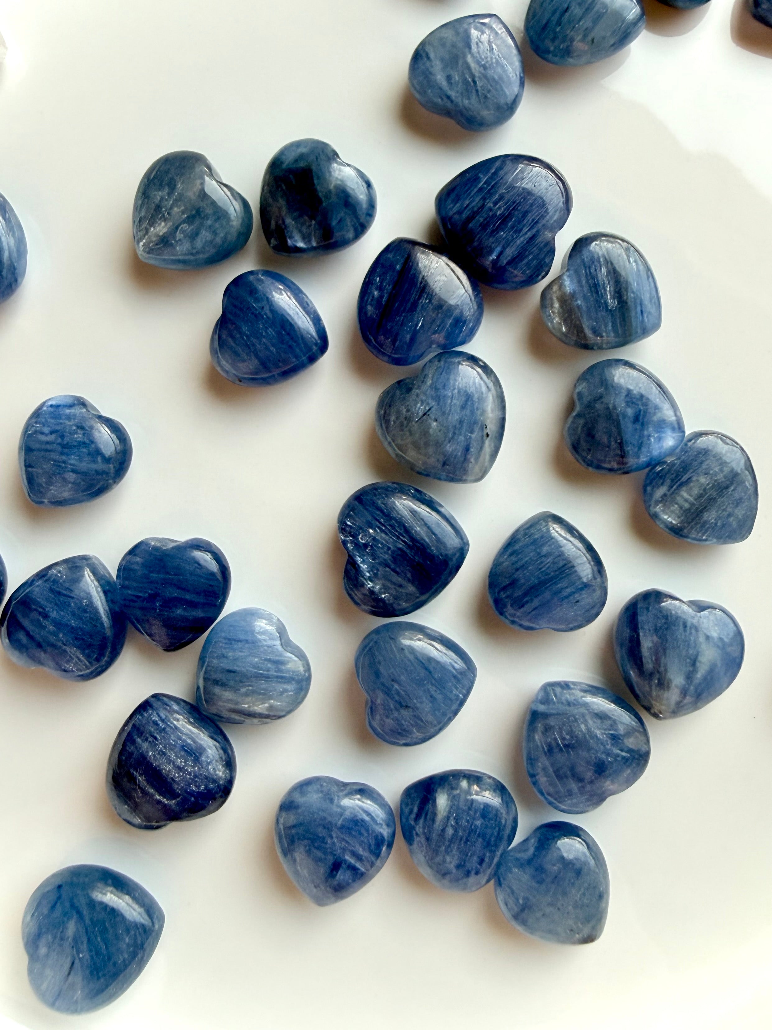 Scattered mini Blue Kyanite heart crystals on white background showing natural variation in color, shimmer and inclusions