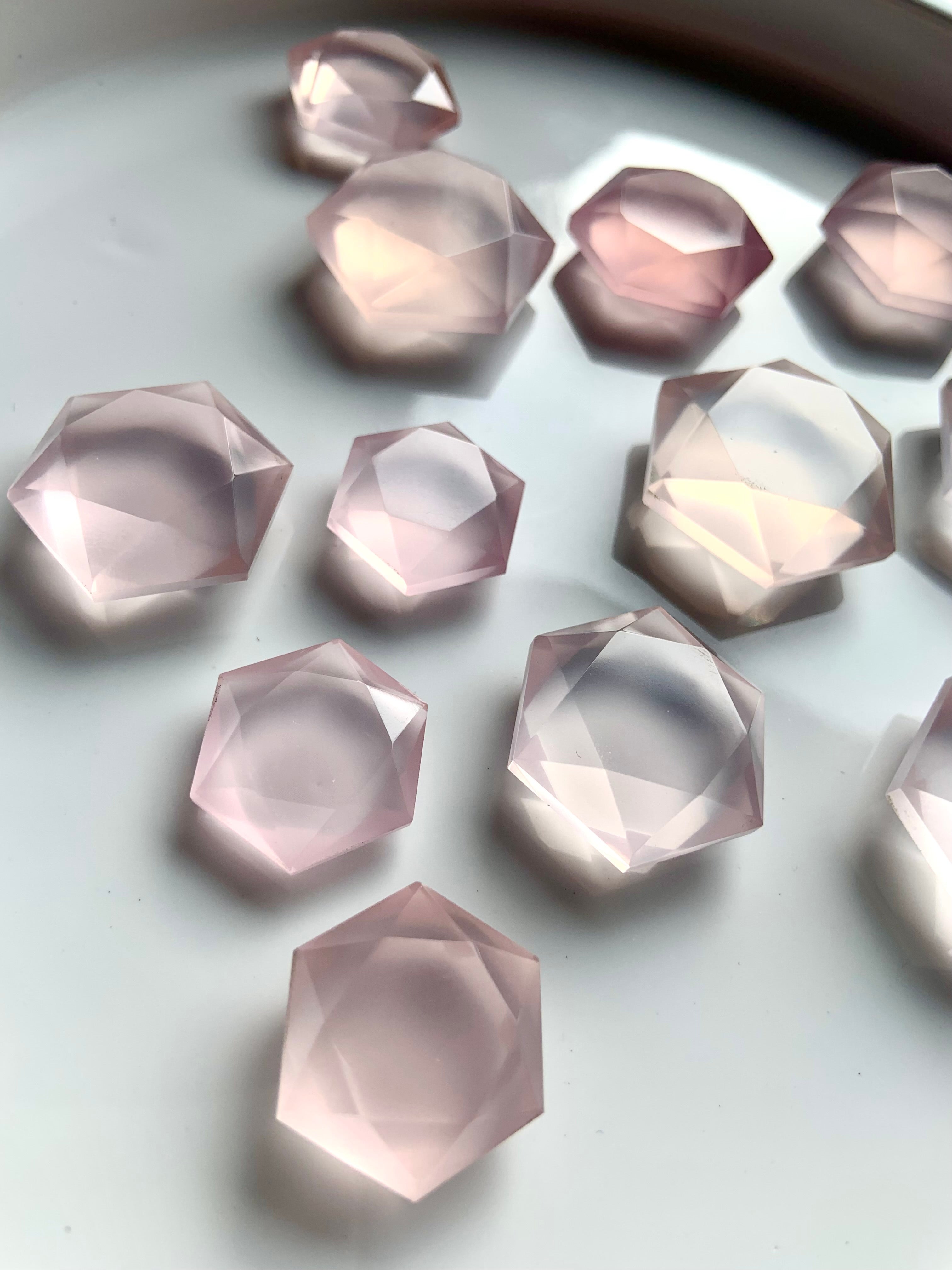 Faceted pink Rose Quartz hexagon crystals in mixed sizes on white plate, luminous sacred geometry gems for Heart Chakra healing