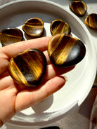 Two Tiger’s Eye heart worry stones with luminous golden bands, photographed in sunlight to highlight their silky reflective finish