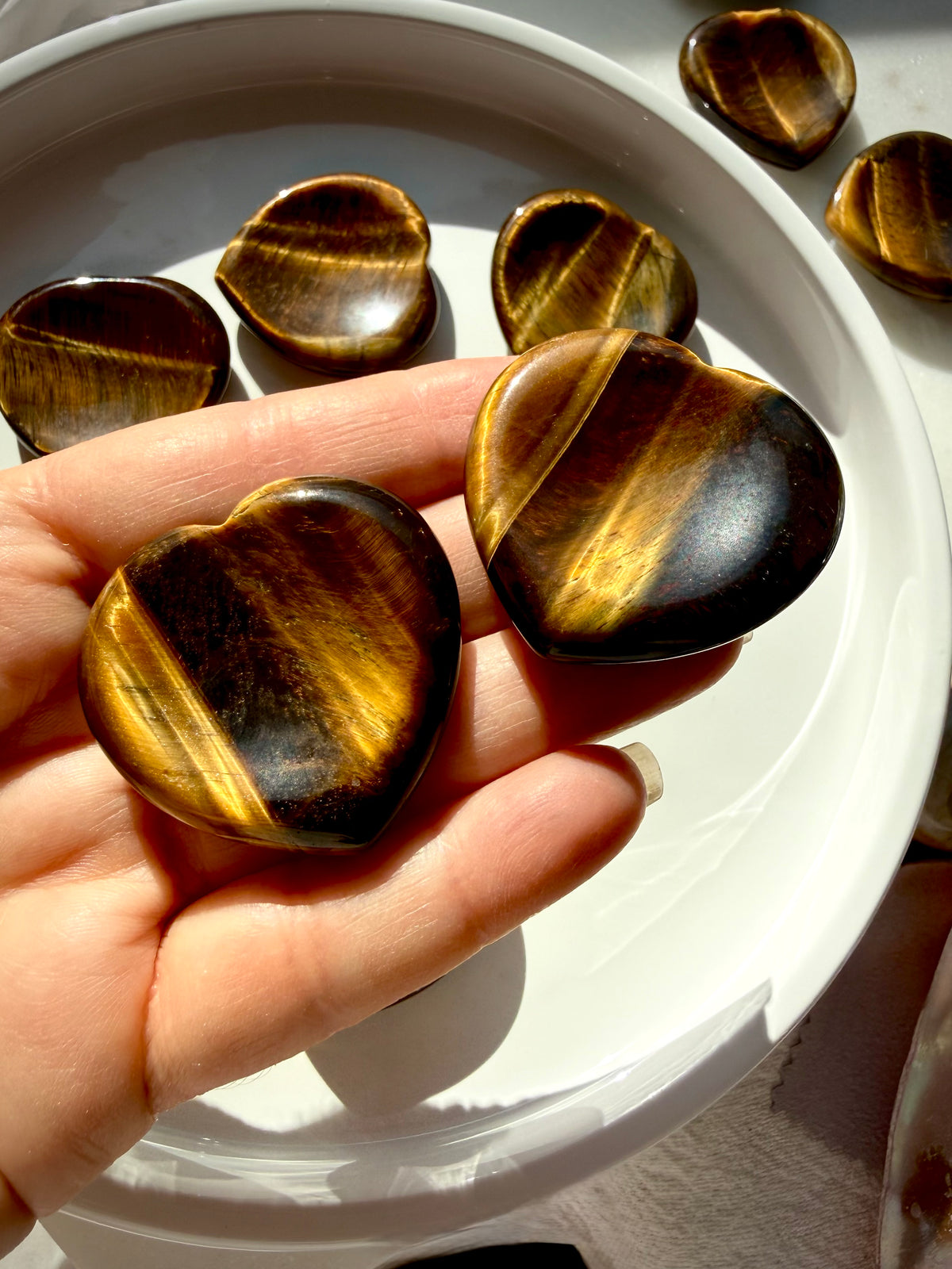 Two Tiger’s Eye heart worry stones with luminous golden bands, photographed in sunlight to highlight their silky reflective finish