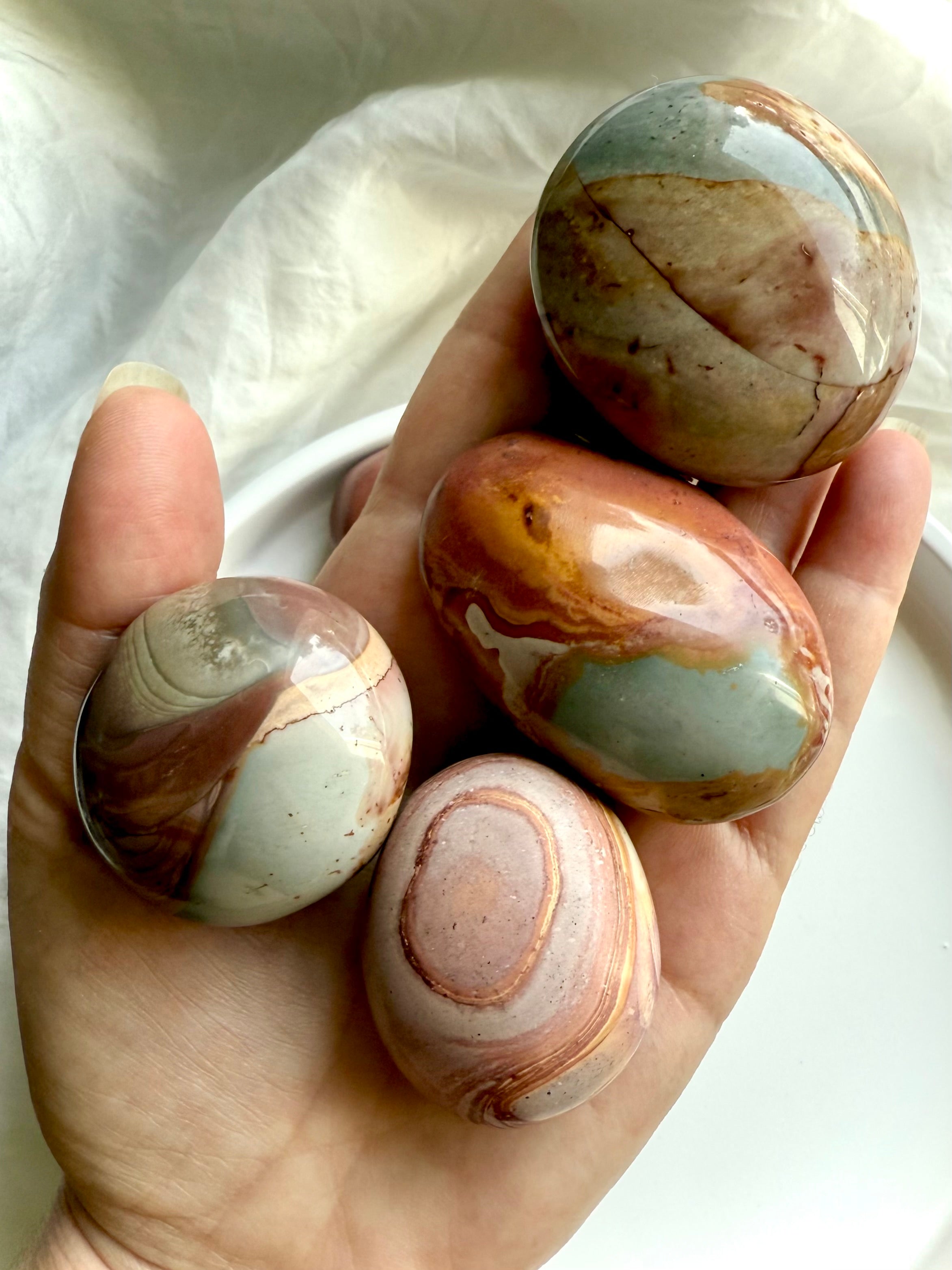Polychrome Jasper palm stones shown in hand, highlighting size variety & earthy, grounding energy. 