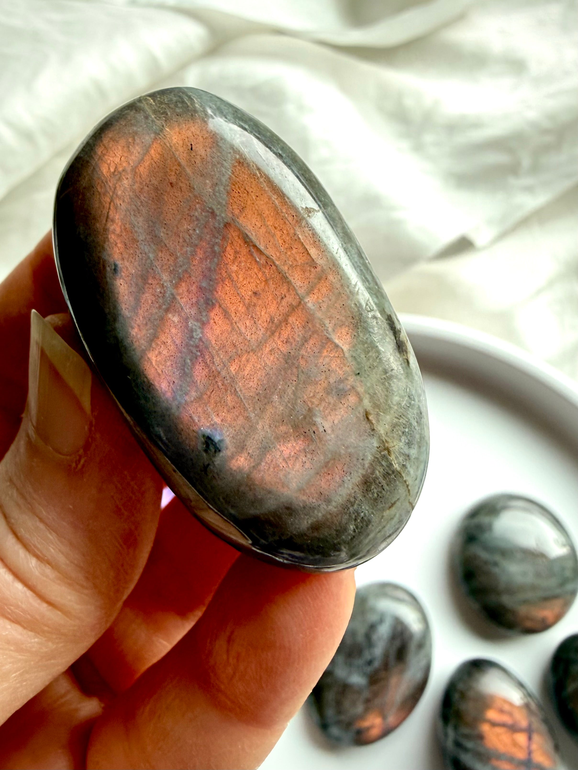 Peach Labradorite palm stone with warm pink and apricot flash held in hand