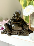 Golden Sheen Obsidian Buddha statue on crystal altar with flower decor – crystal carving for protection, abundance, and solar plexus healing