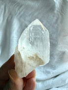 Natural Lemurian Quartz crystal point held in hand with rough matrix, cloudy inclusions, and distinctive growth markings