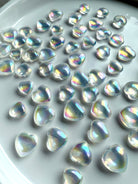 Angled view of iridescent mini aura quartz hearts glowing with rainbow light, displayed on white ceramic plate