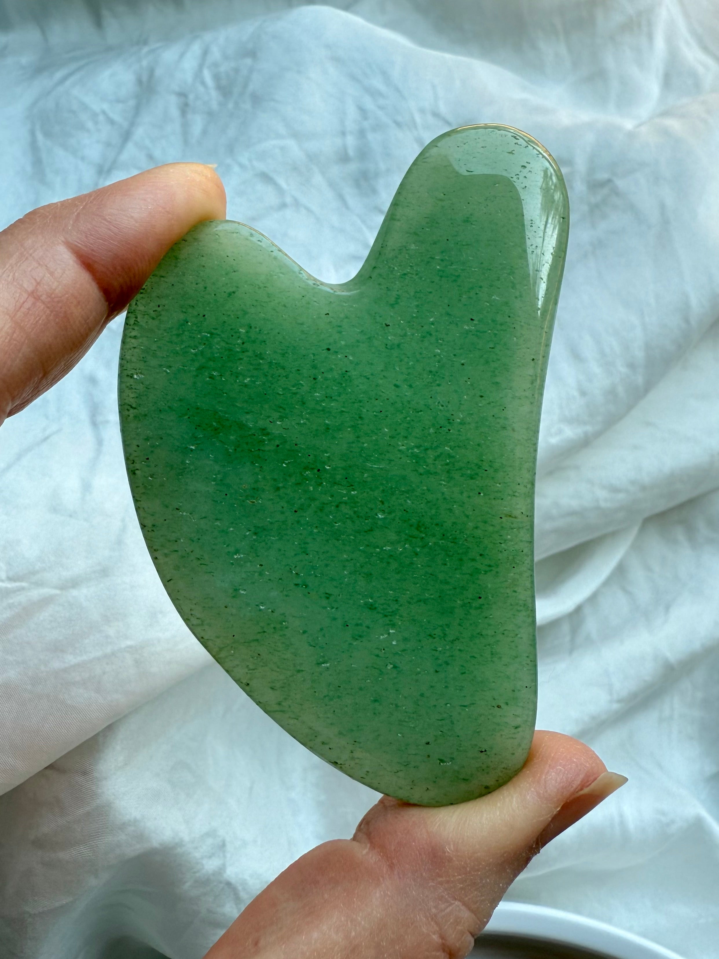 Green Aventurine crystal gua sha facial massage tool held upright against white fabric background