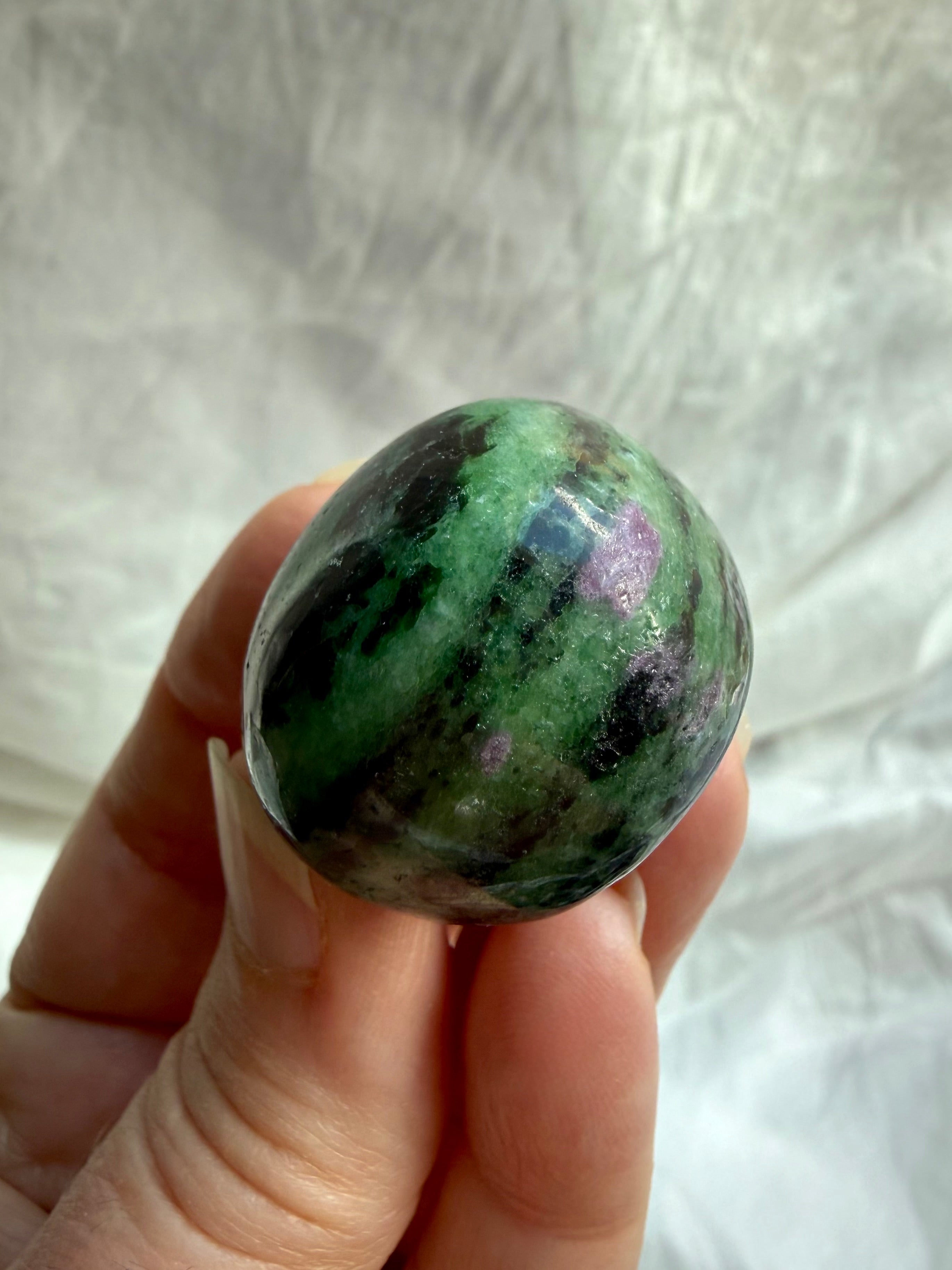 Close-up of polished Ruby Zoisite gemstone showing vibrant green and pink mineral formations with natural black inclusions