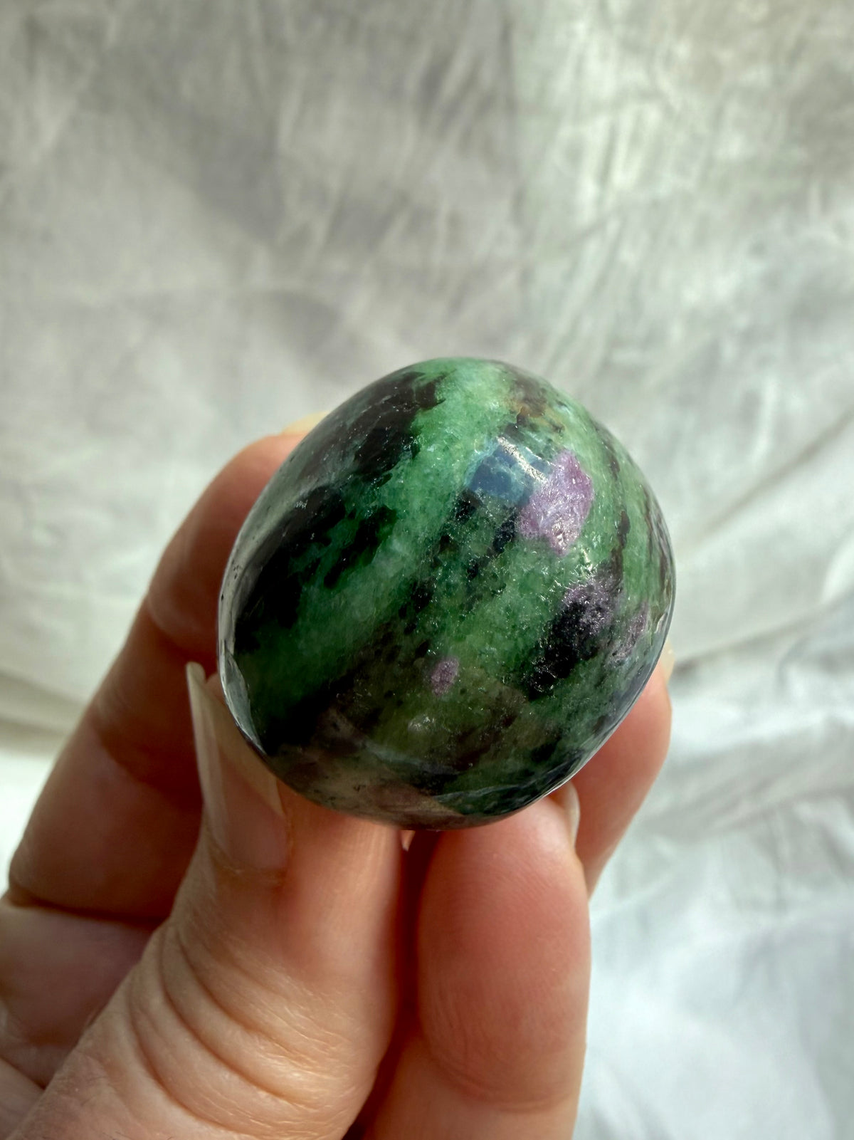 Close-up of polished Ruby Zoisite gemstone showing vibrant green and pink mineral formations with natural black inclusions