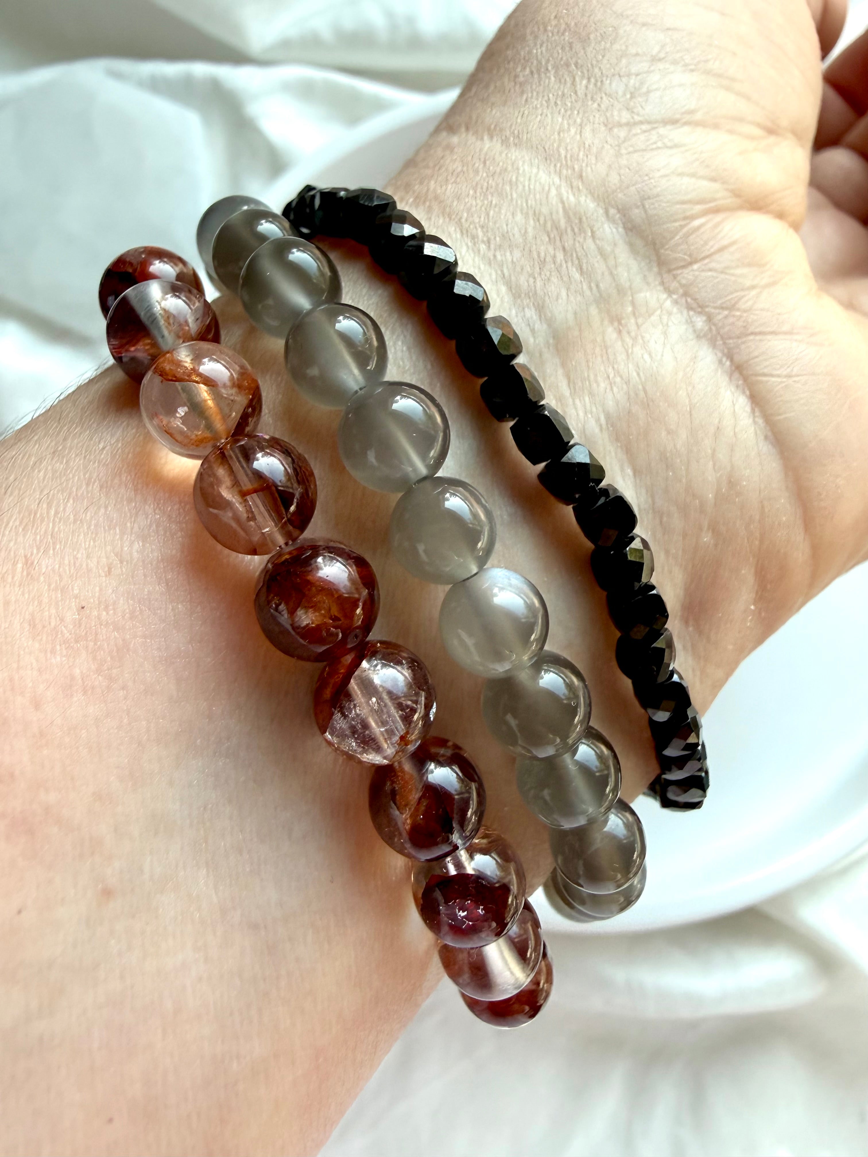 Black Moonstone, Fire Quartz and faceted Black Spinel crystal bracelets worn together, showing contrasting gemstone colors and bead styles