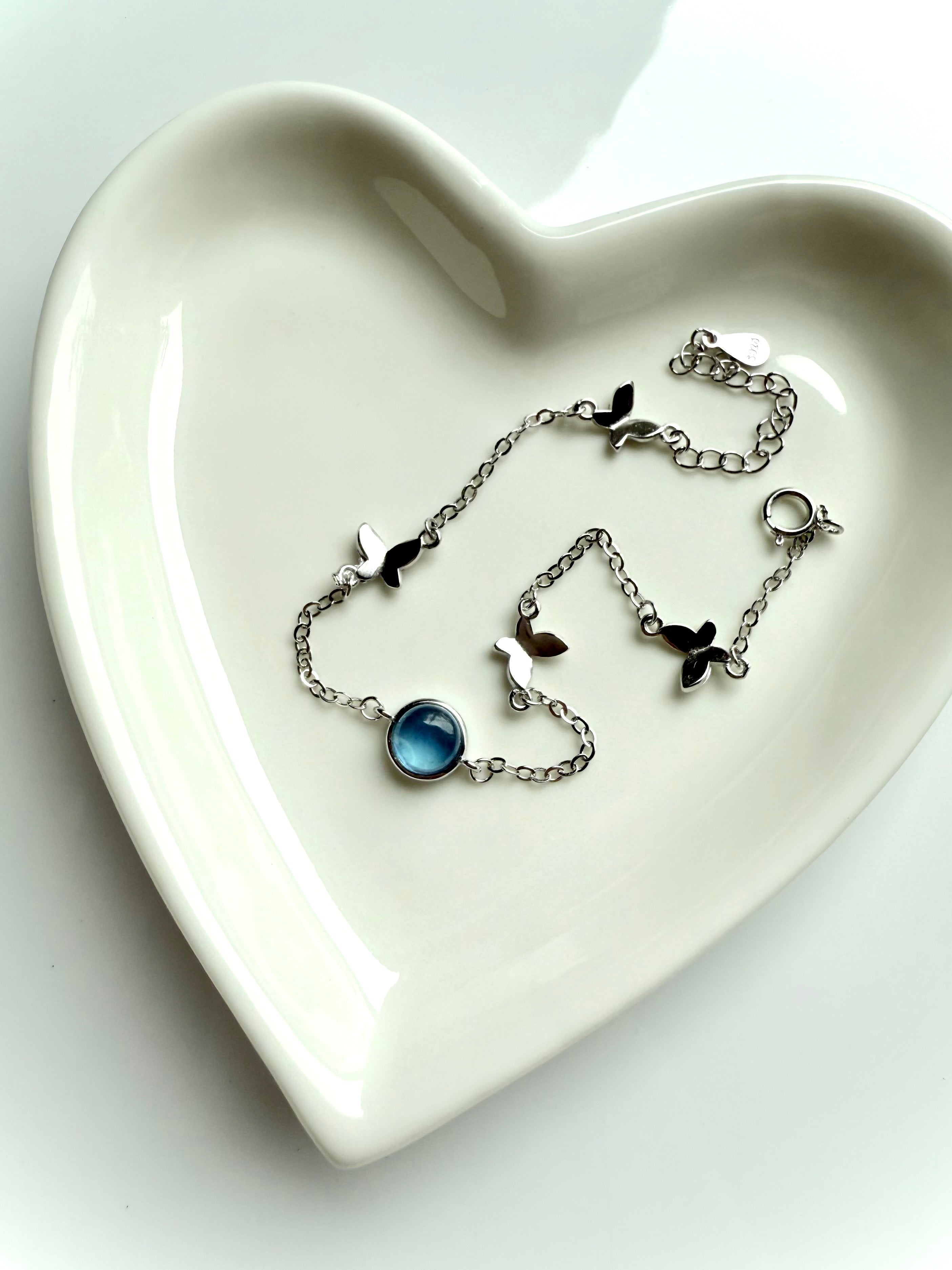 Dainty sterling silver aquamarine butterfly bracelet with heart chakra energy, styled in heart-shaped dish for gift-ready presentation