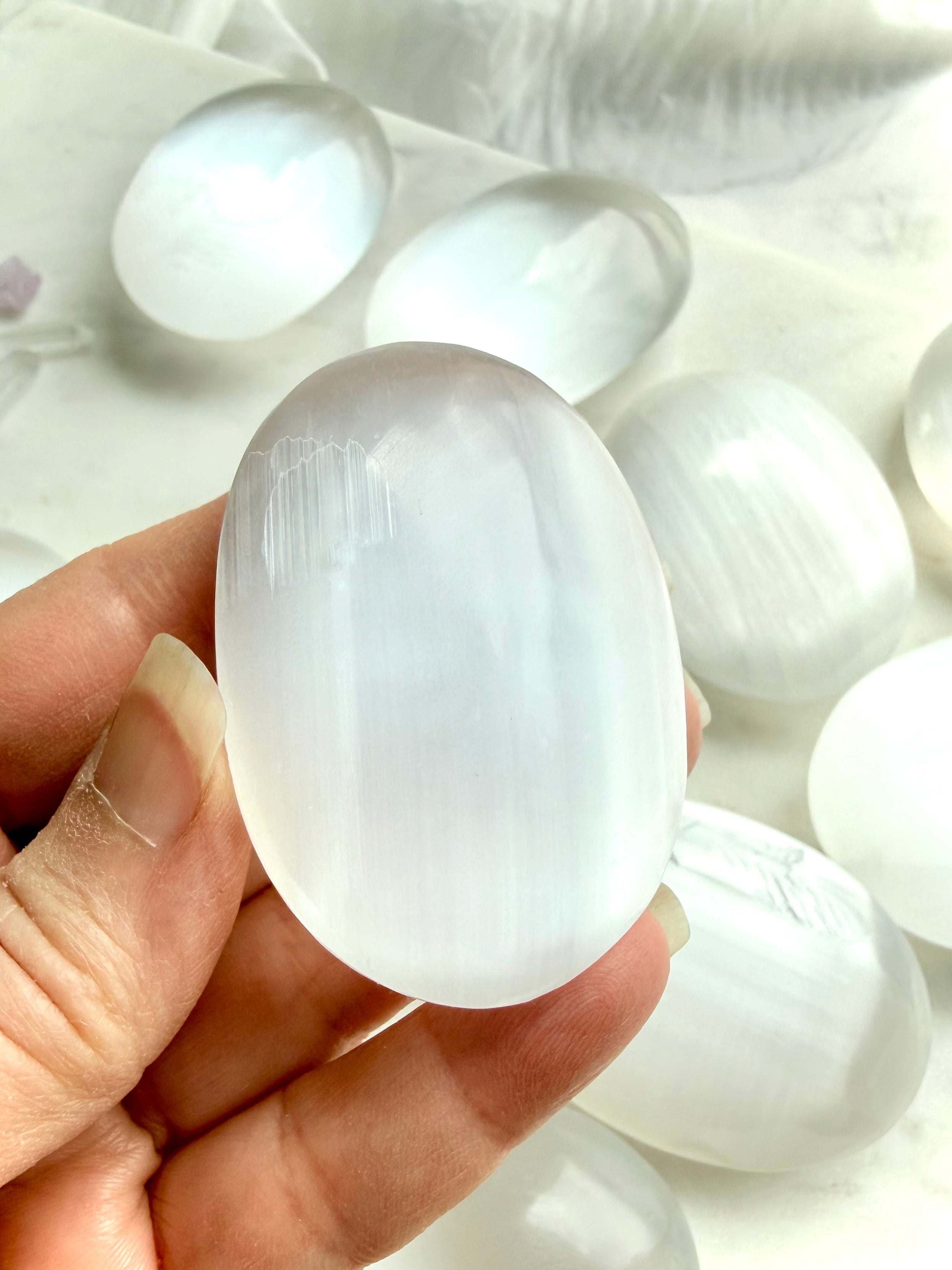 Selenite palm stone close-up highlighting silky luster, flowing linear patterning, and polished glossy surface
