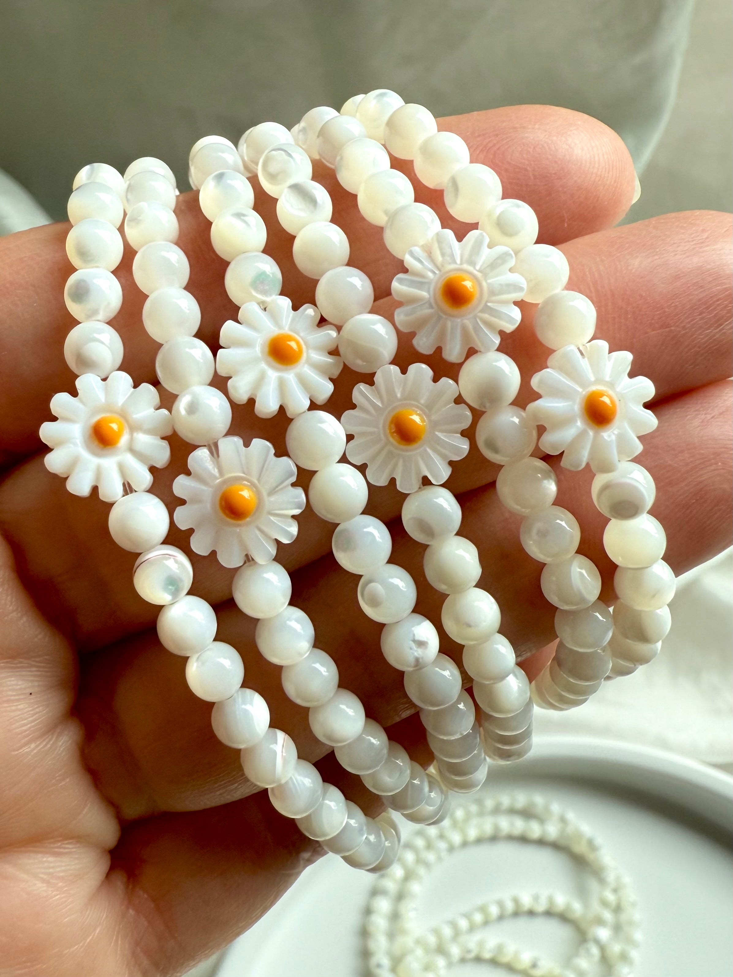 Hand holding boho-style Mother of Pearl daisy bracelets with natural white gemstone beads and carved flower accents, stacked for a whimsical and lighthearted crystal jewelry look
