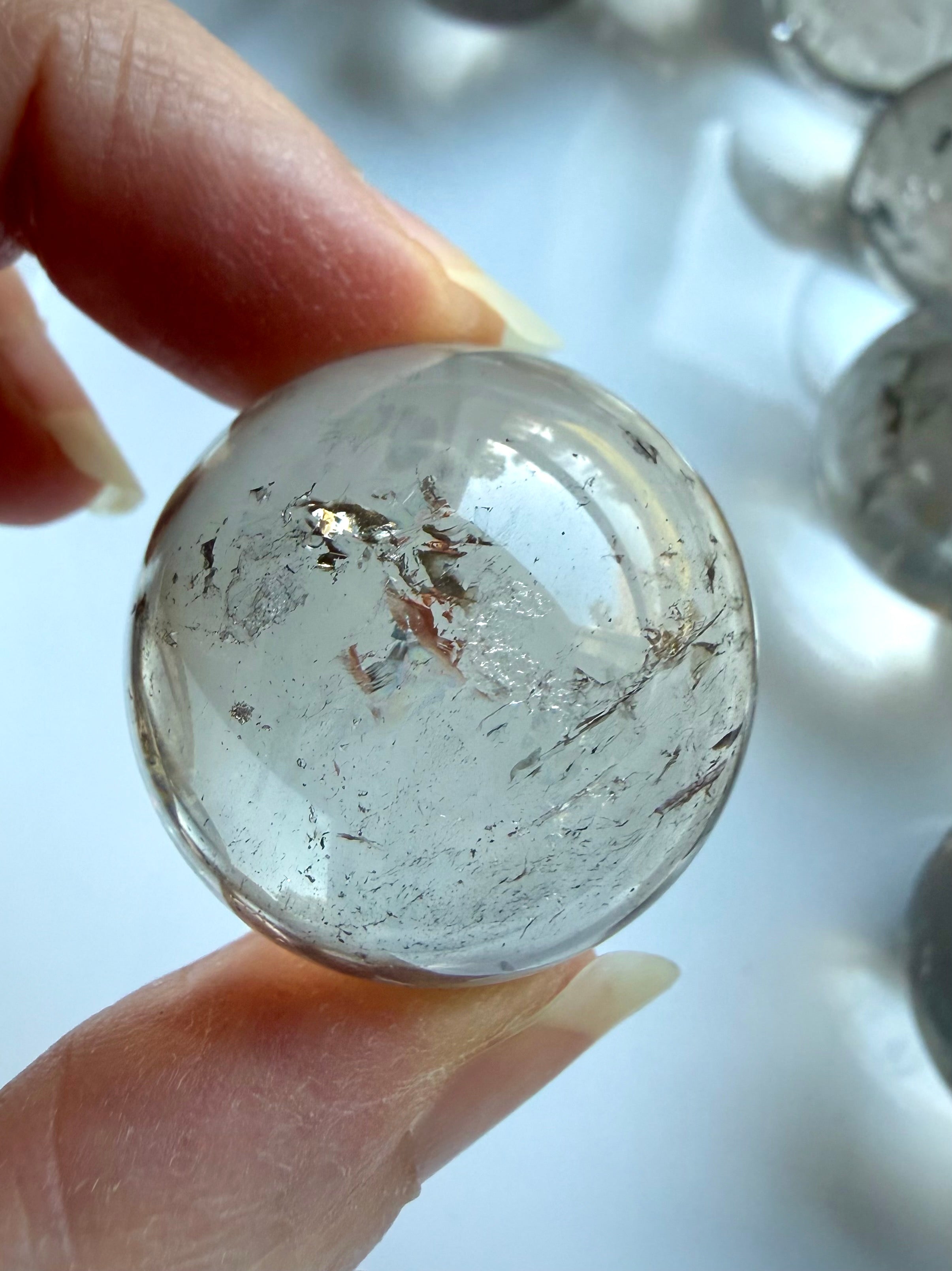 Small Smoky Quartz sphere held between fingers showing soft translucent smoky color and inclusions