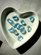 Aquamarine Mini Moons in white heart bowl in bright natural light — celestial crystal carvings in luminous blue hues