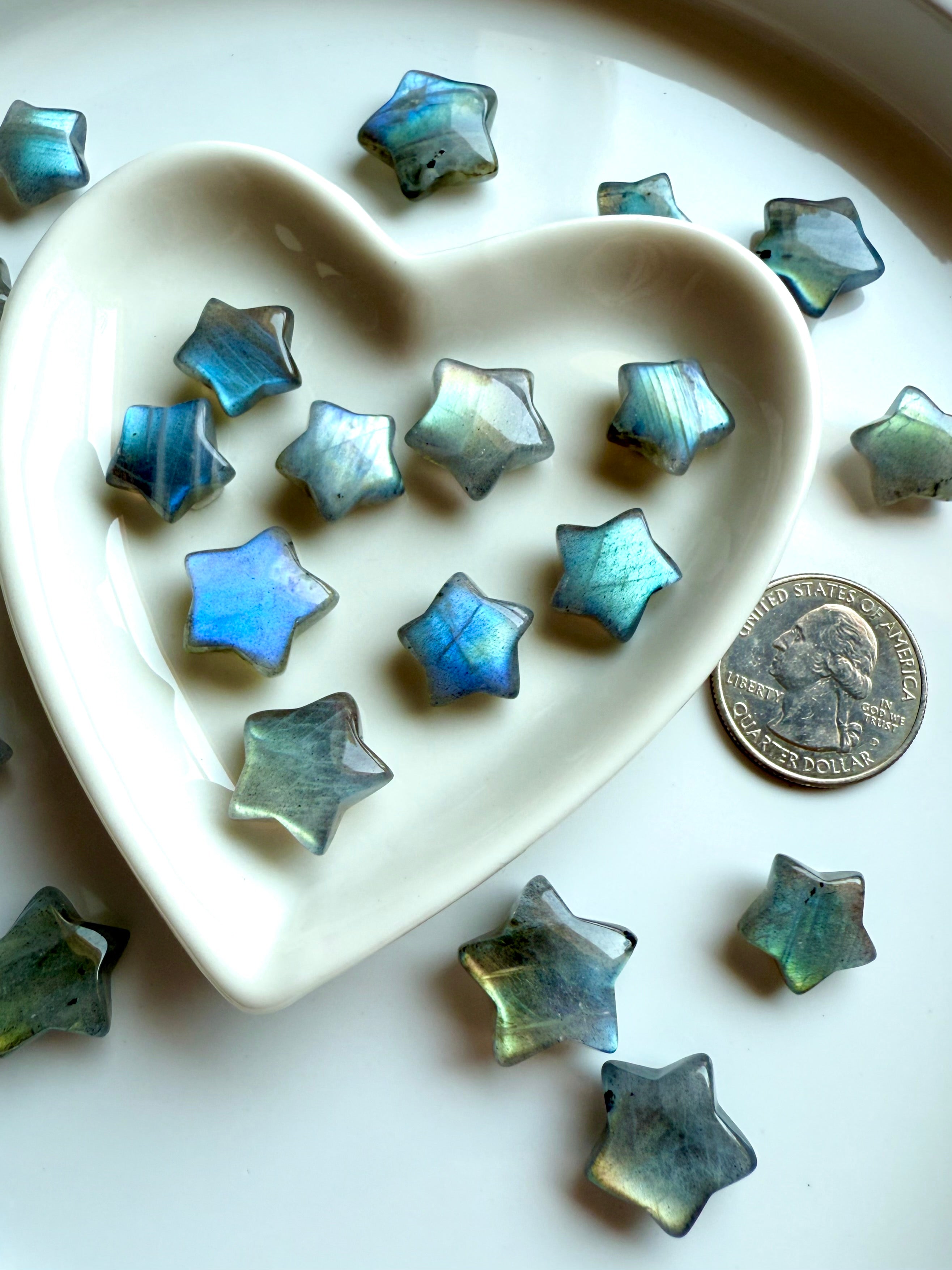 Angled shot of pastel Labradorite stars in a heart-shaped bowl with a quarter for scale — mini crystal stars for gentle protection & spiritual balance.
