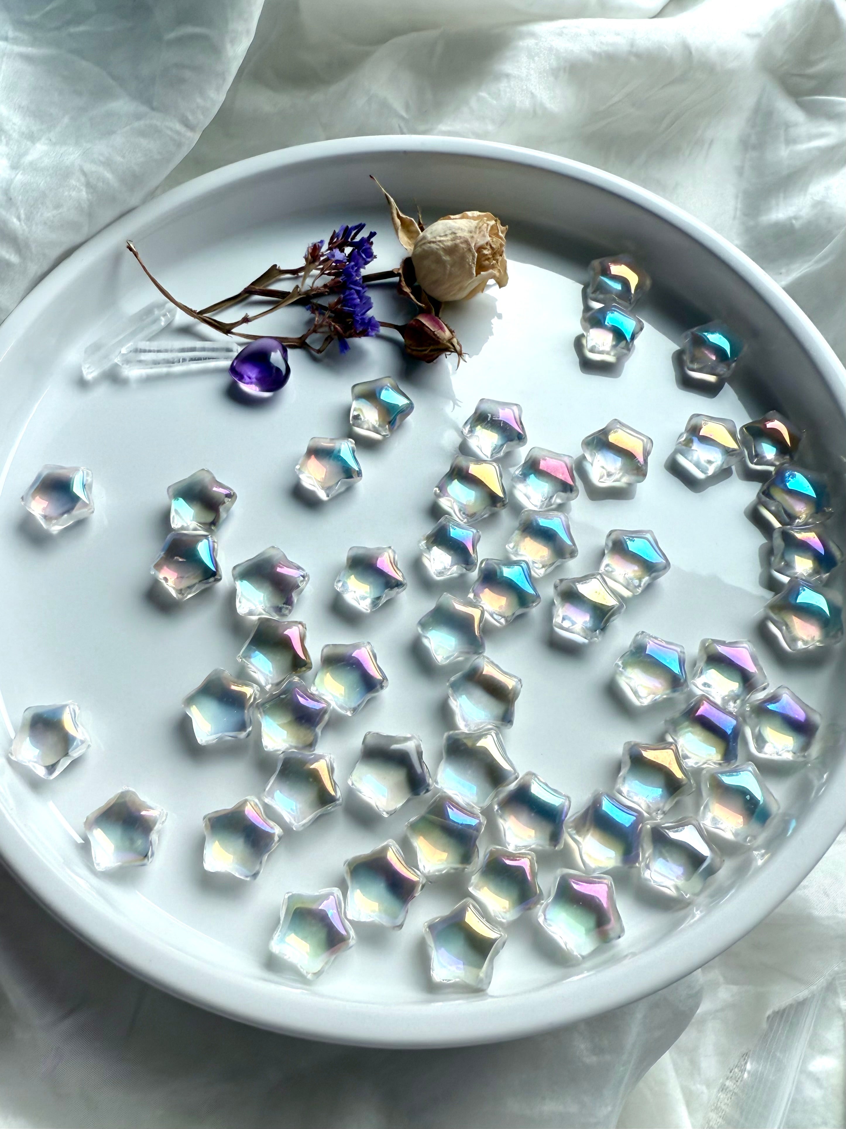 Opalescent mini aura quartz stars with rainbow sheen displayed on white tray with dried flowers, amethyst heart, and quartz points — healing crystals for universal chakra balance. 